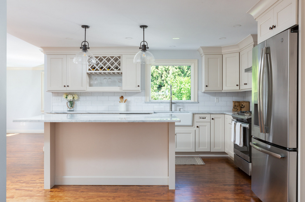 Bright modern kitchen with white cabinets, island, stainless steel fridge, and hardwood floors
