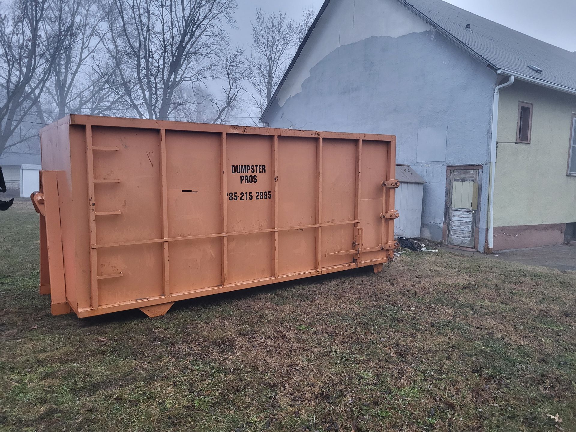 A large black dumpster is sitting in the middle of a dirt field.