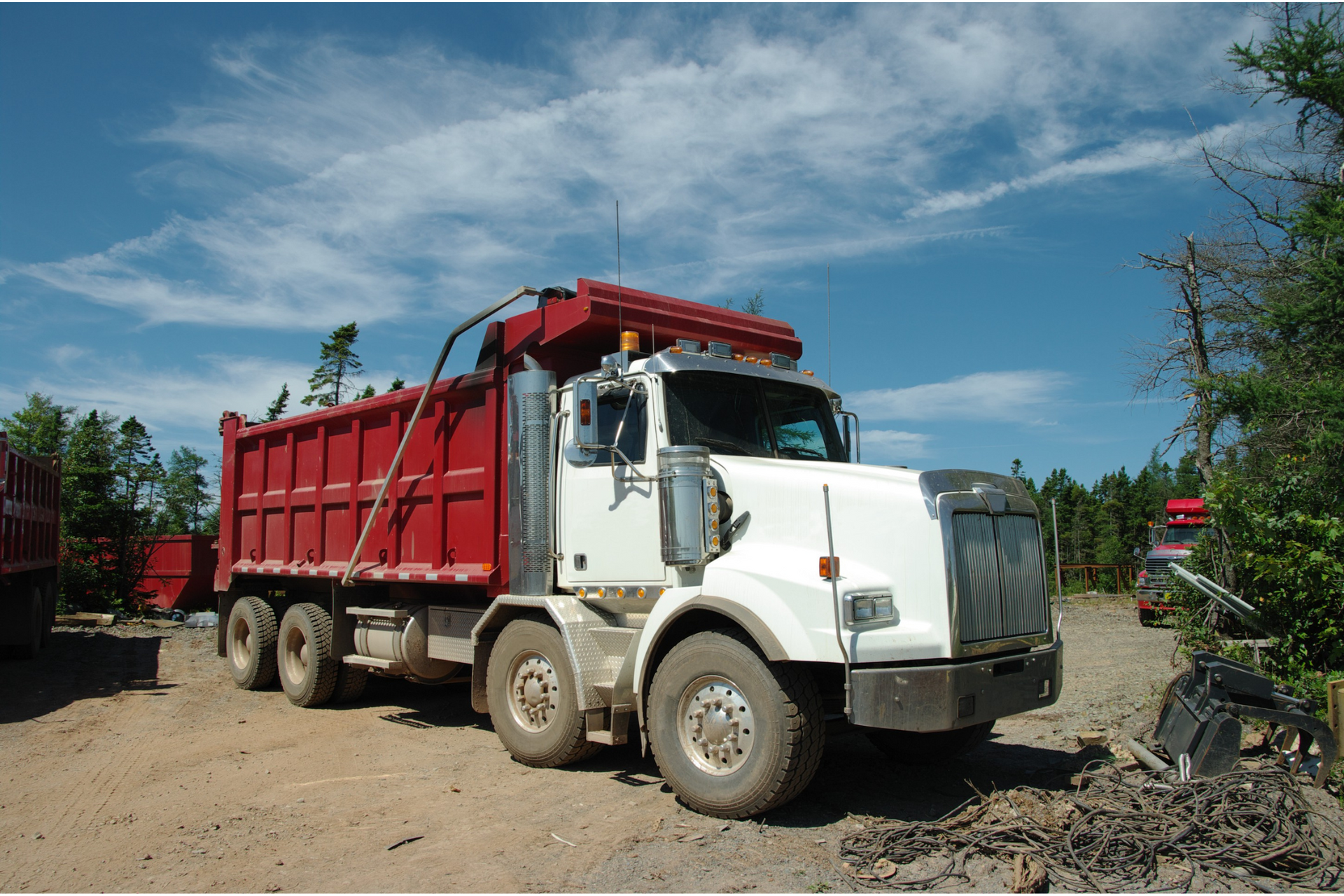 A white dump truck with a red roof is parked in a dirt lot