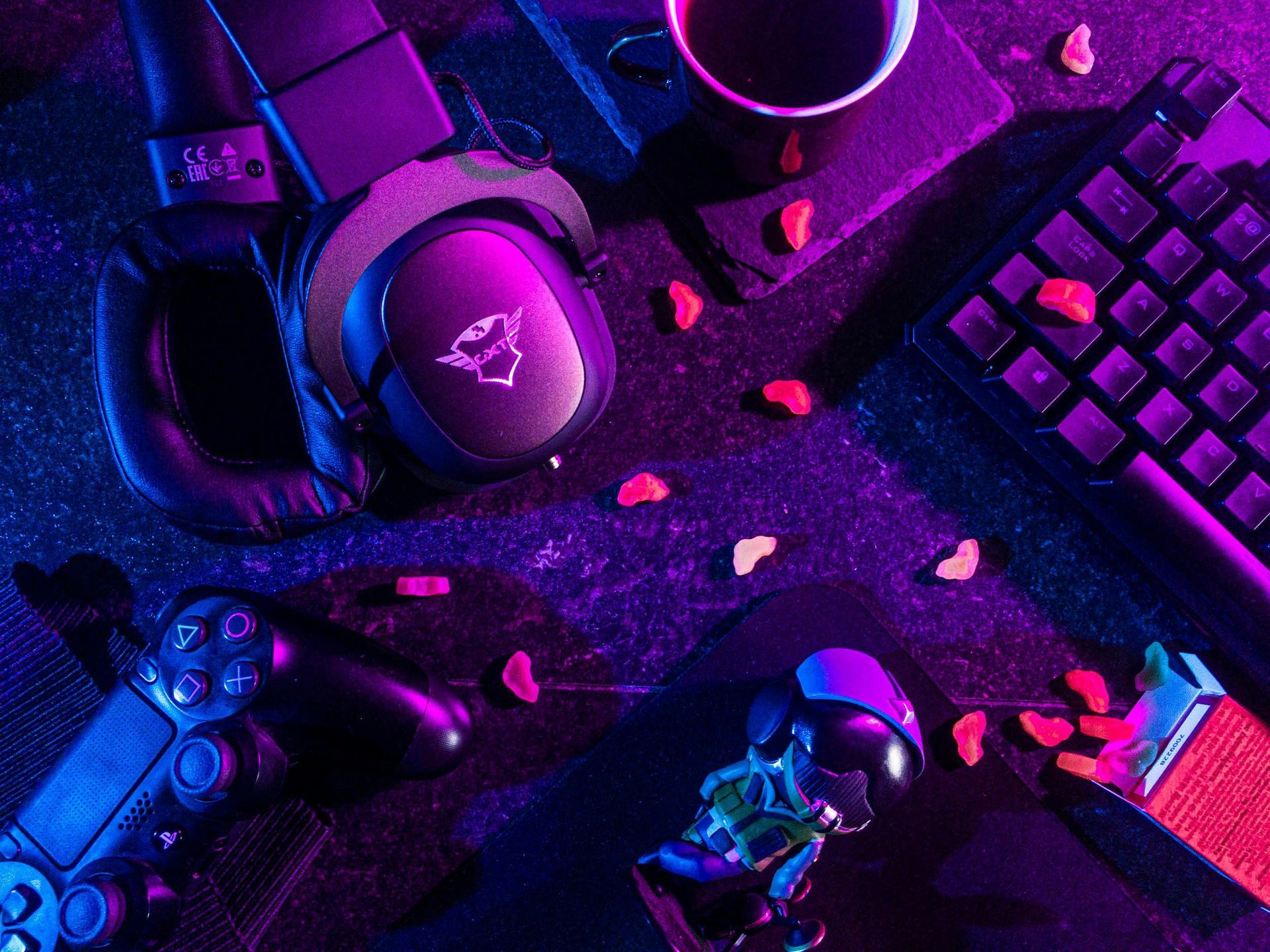A video game controller , keyboard , headphones , and a cup of coffee are on a table.