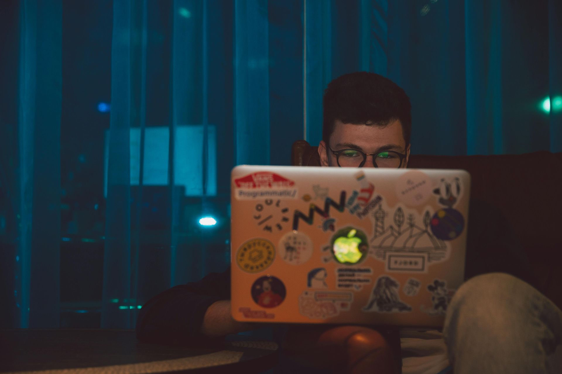 A man is sitting in front of a laptop computer with stickers on it.