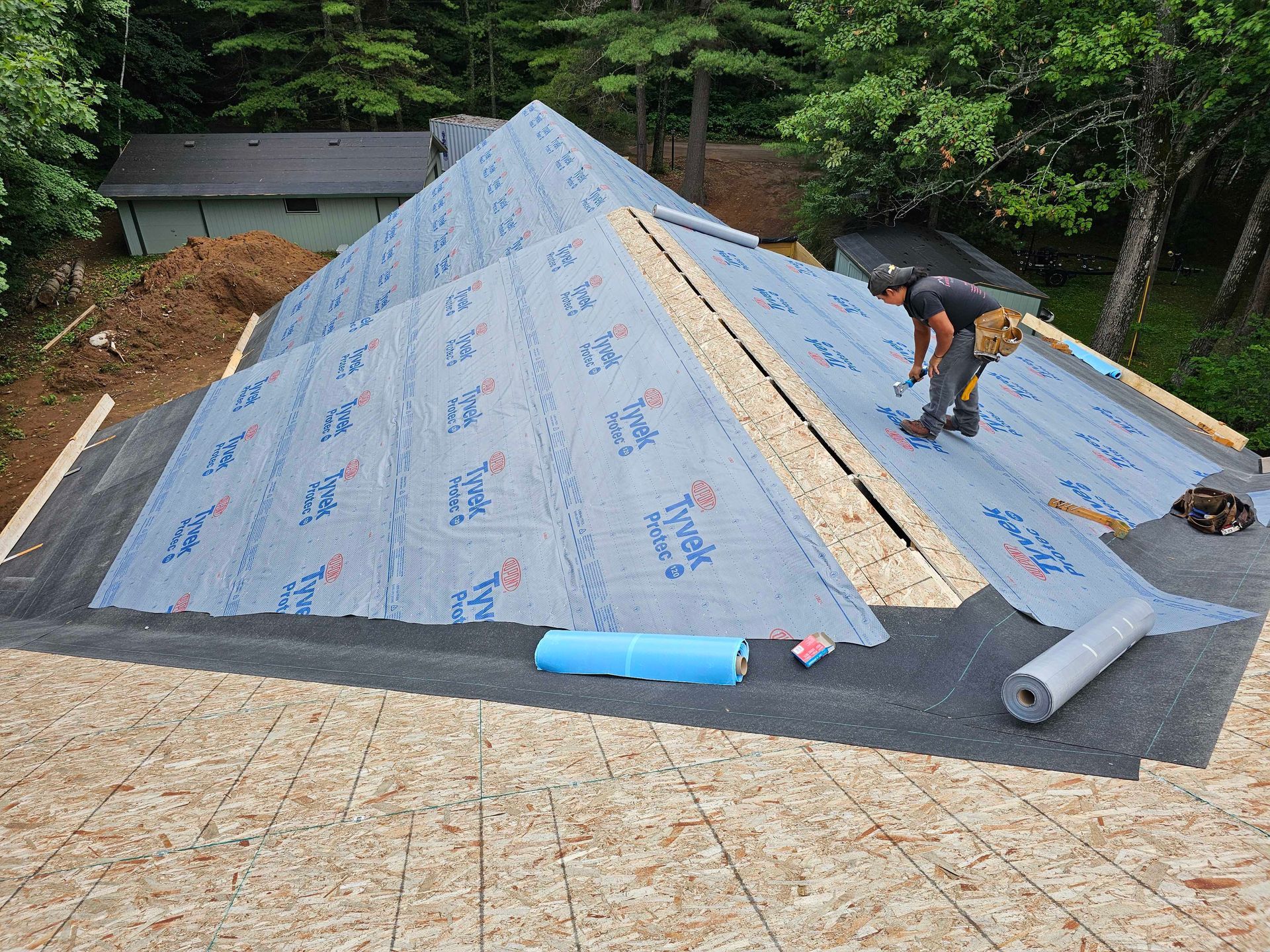 A man diligently repairs a roof, hammer in hand, surrounded by tools and roofing materials.