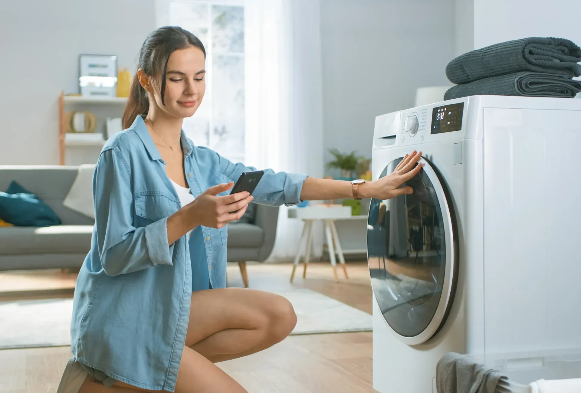 A man is kneeling down in front of a washing machine in a kitchen.