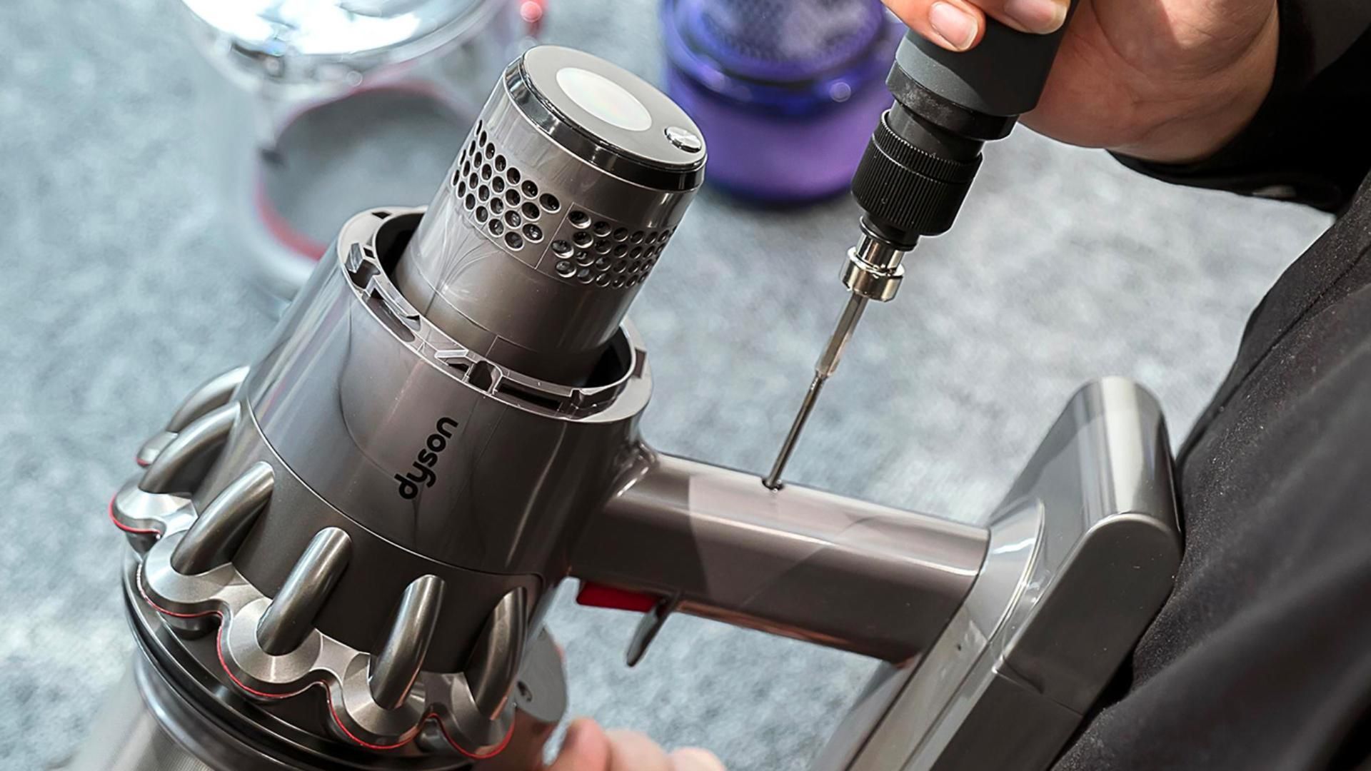 A person is using a drill to fix a dyson vacuum cleaner.