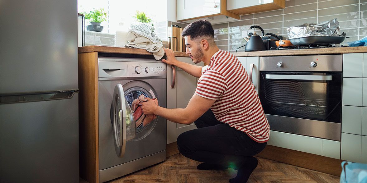 A man is kneeling down in front of a washing machine in a kitchen.