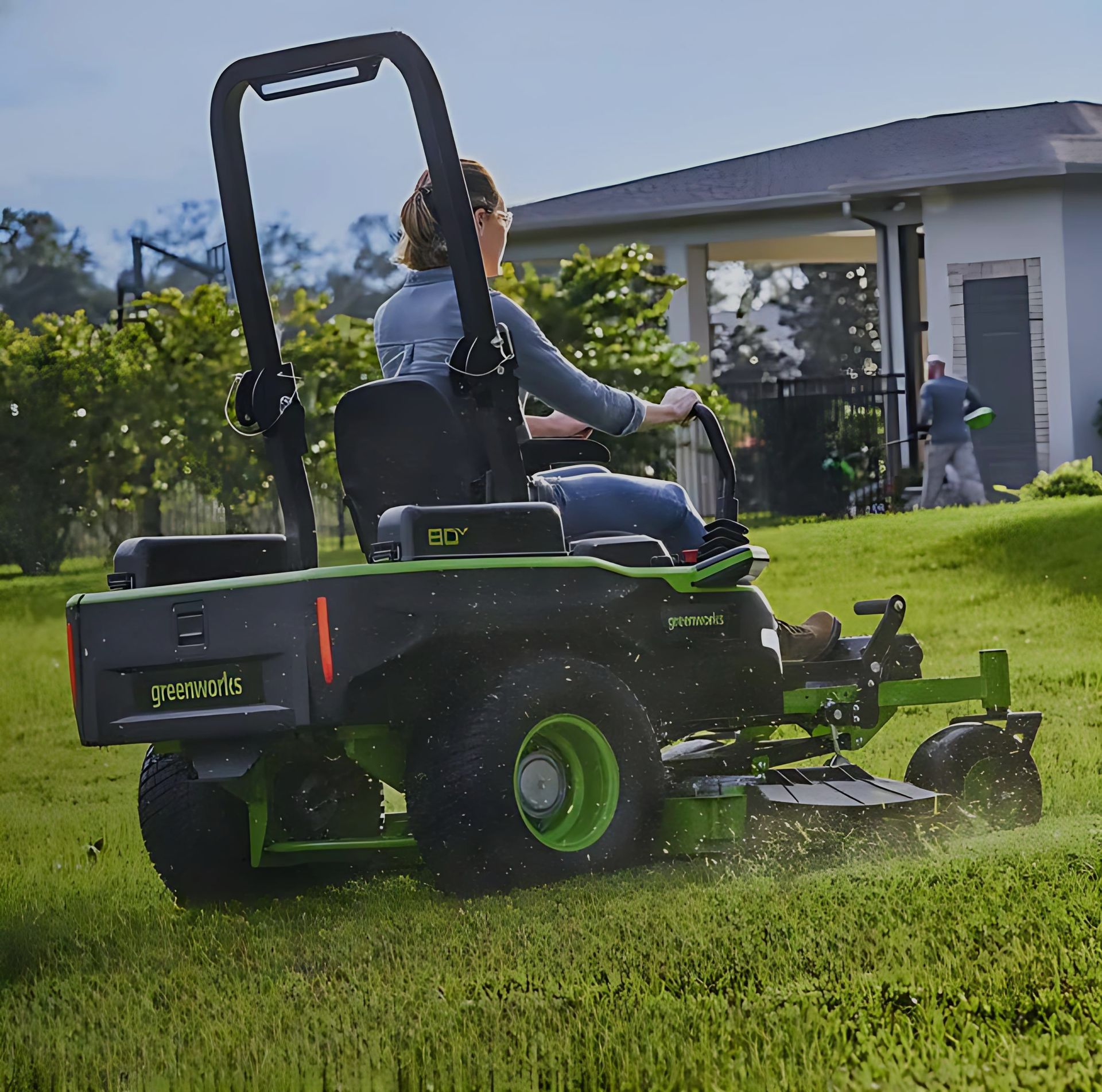 Woman On Green Riding Lawnmower, Cutting Grass In A Yard, Sunny Day