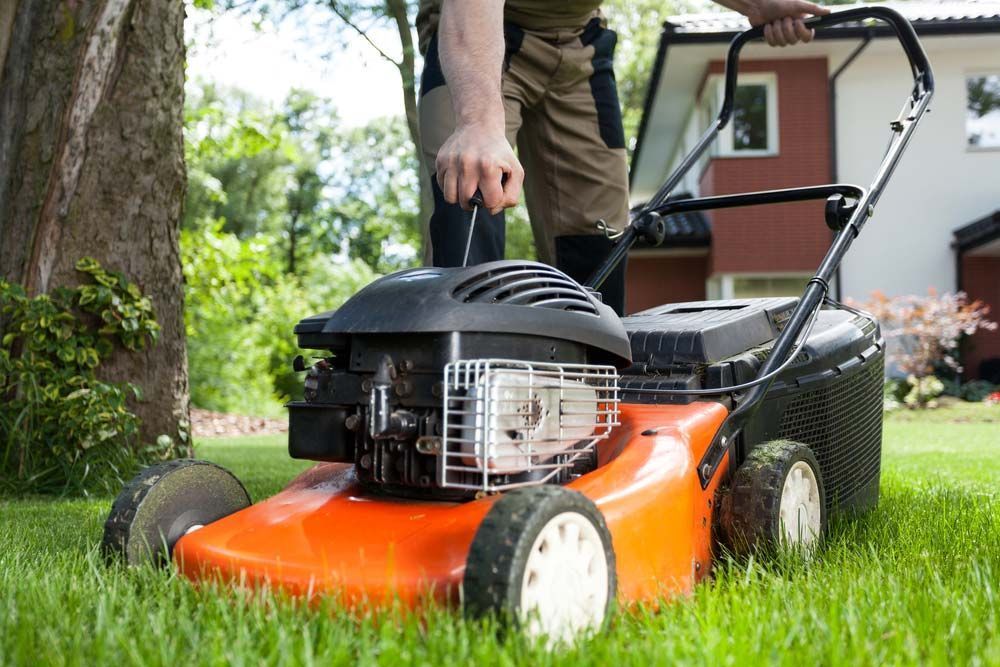 A Man is Using an Orange Lawn Mower to Cut the Grass in Front of a House — Diamond Service Centre In Lismore, NSW