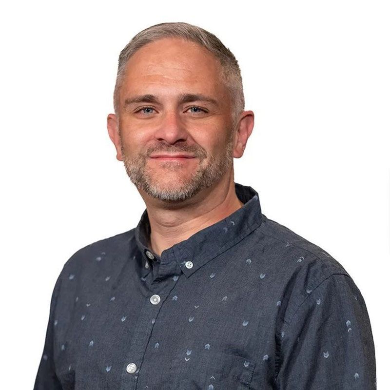 Man with short gray hair and a blue patterned shirt smiling, facing the camera.