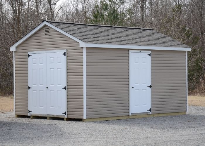 Clay storage shed with white double doors and a single side door on gravel.