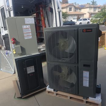Two Trane HVAC units on pallets outside a van, possibly for installation. Gray and black.