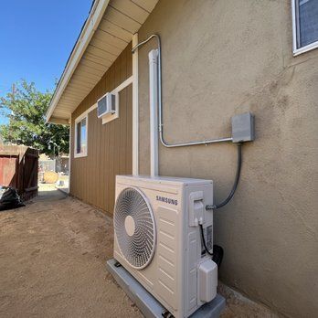 An outdoor air conditioning unit installed on a concrete base, connected to a building with tan siding.