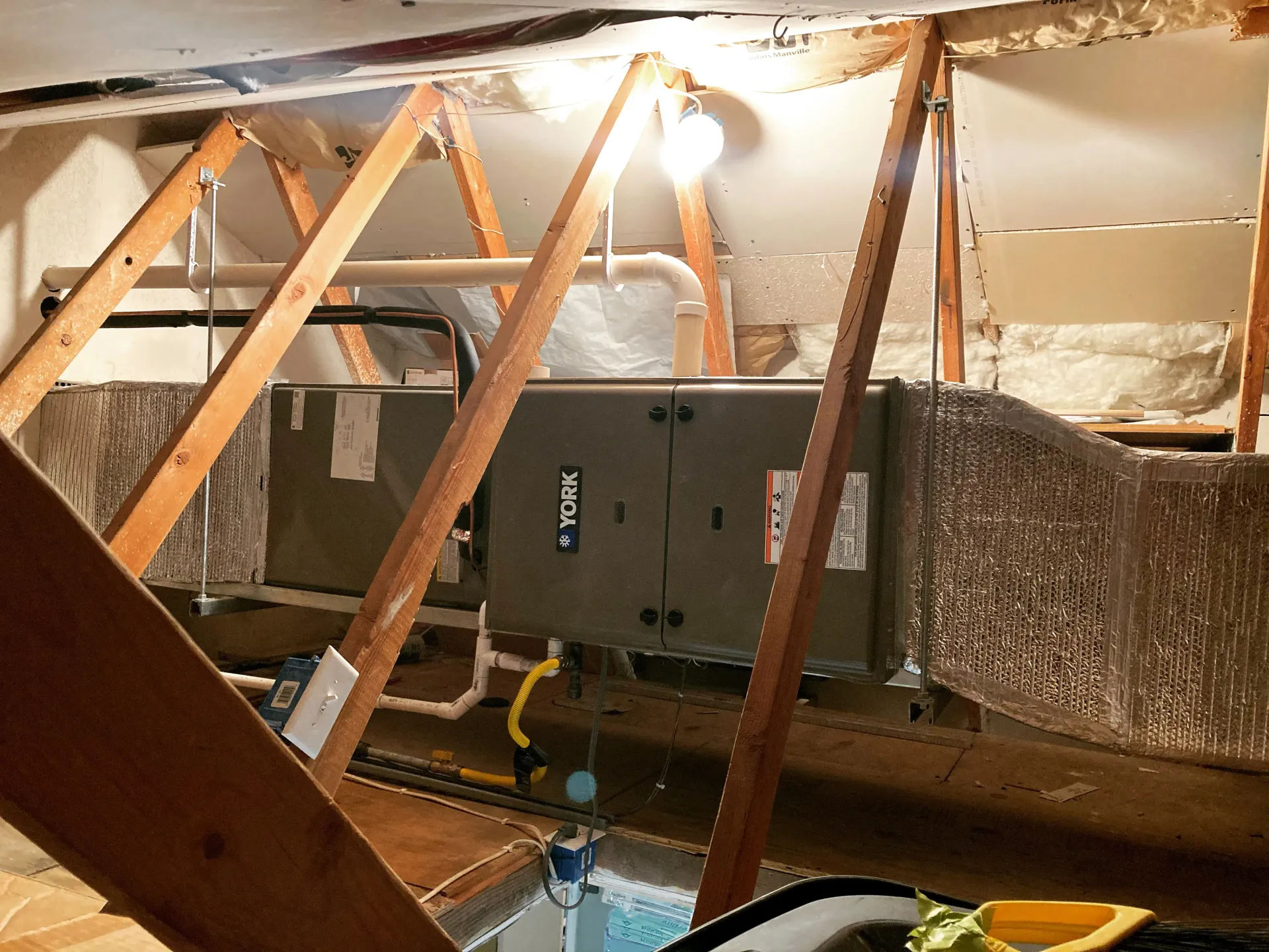 HVAC unit in an attic, surrounded by wooden beams and insulation.