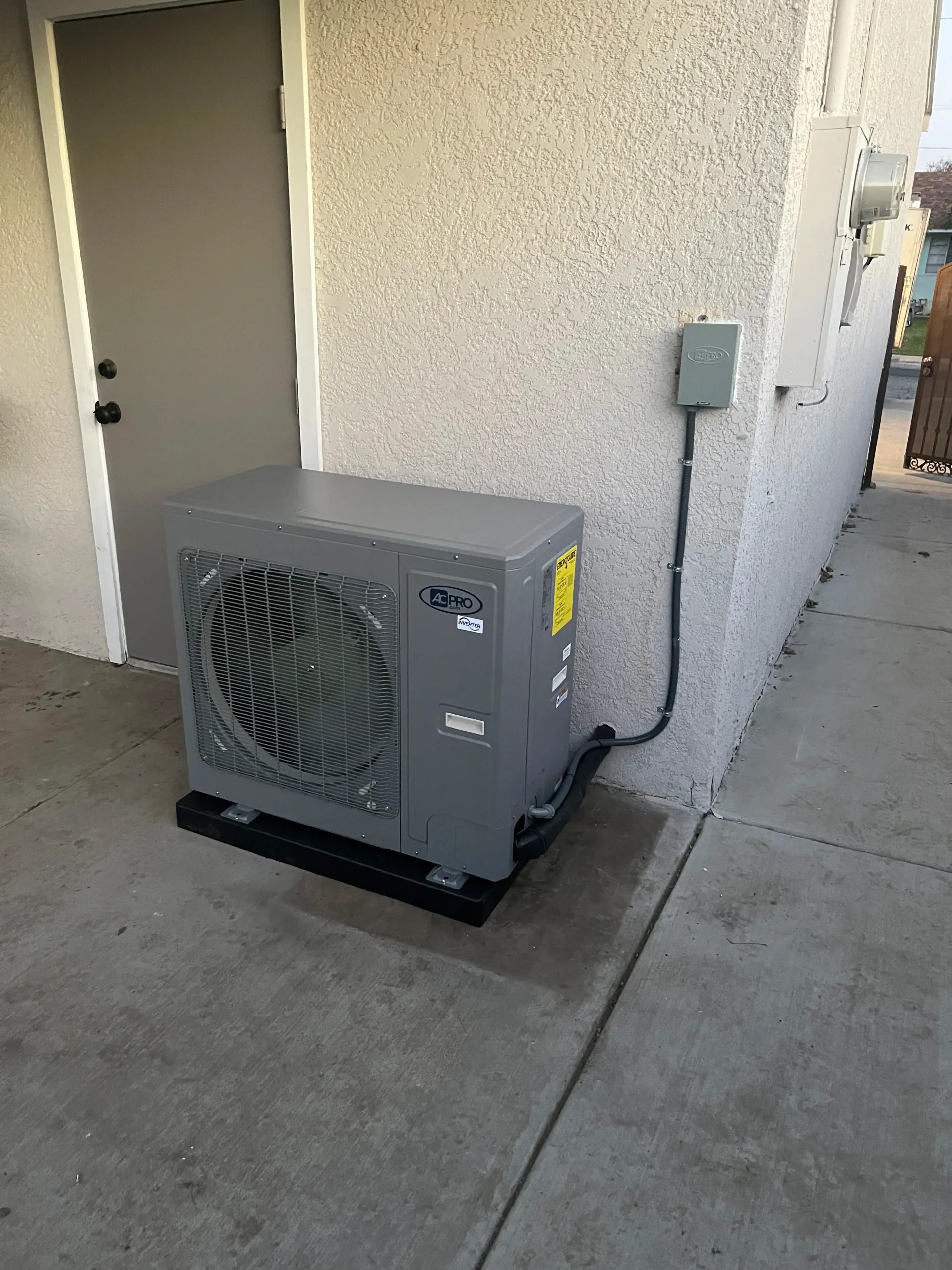 Gray air conditioning unit on a concrete pad next to a stucco wall and door.