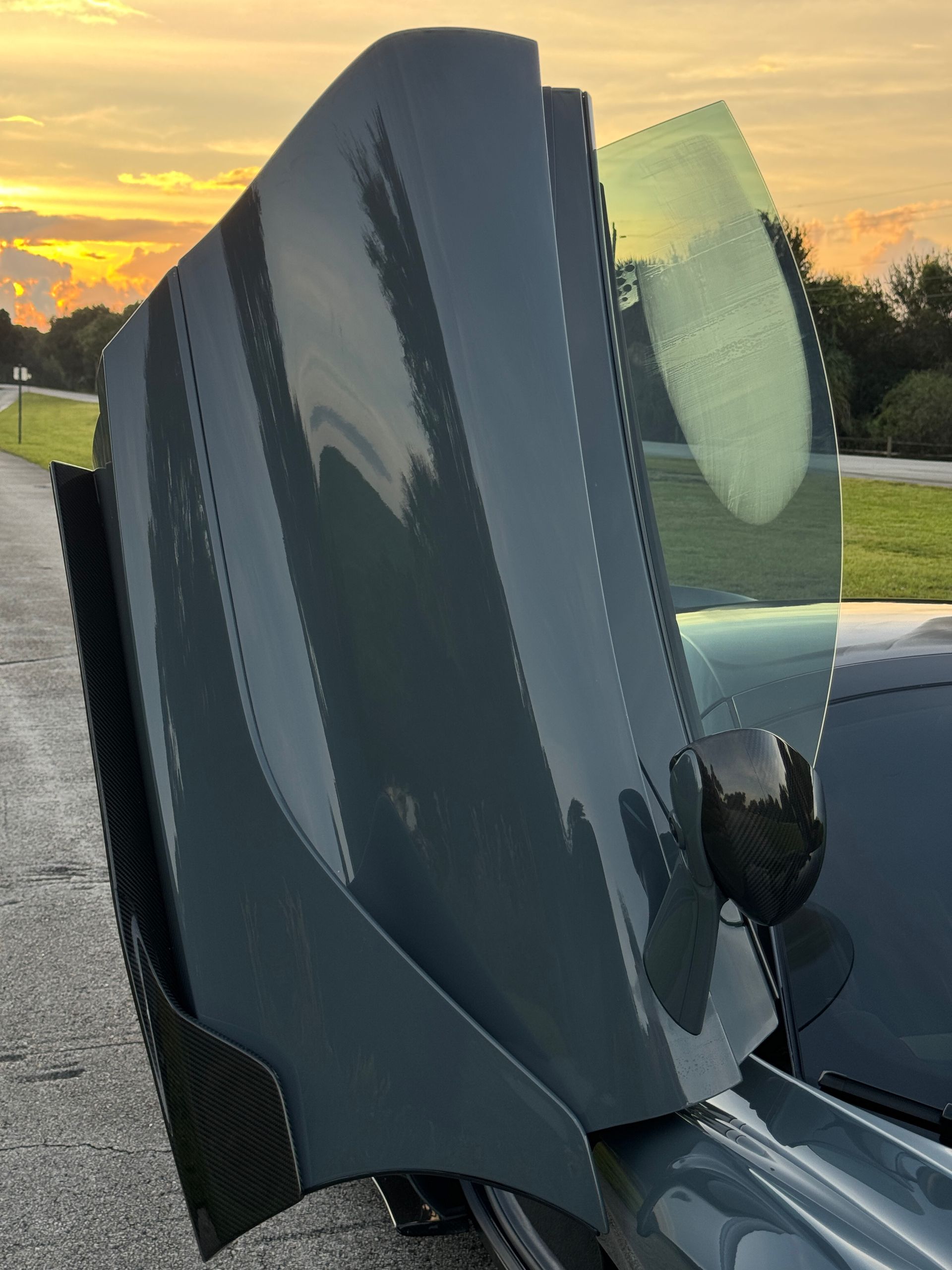Gray sports car door open, with carbon fiber details against a sunset sky.