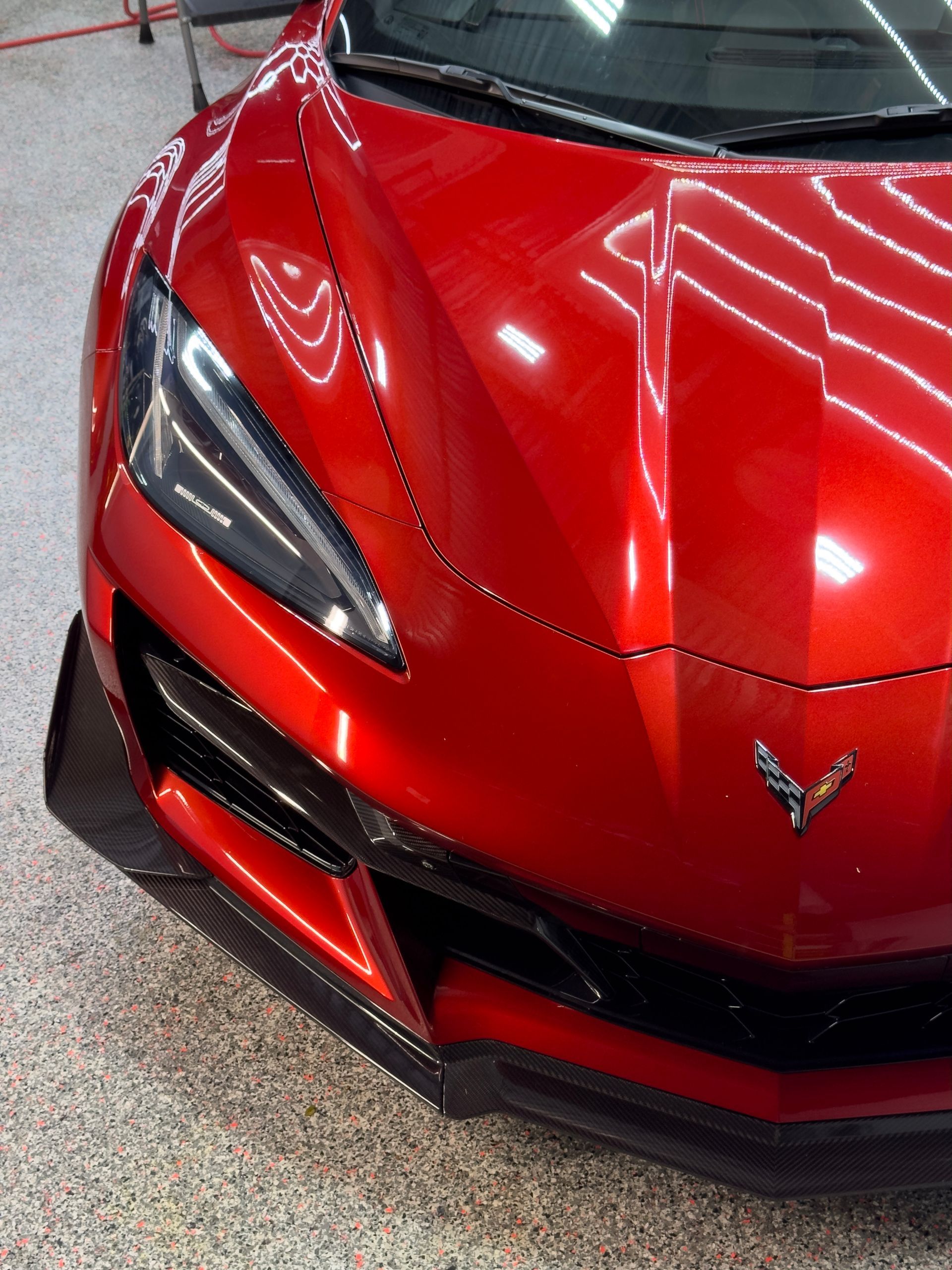 Red sports car's front with a black trim and a Corvette emblem, parked indoors.