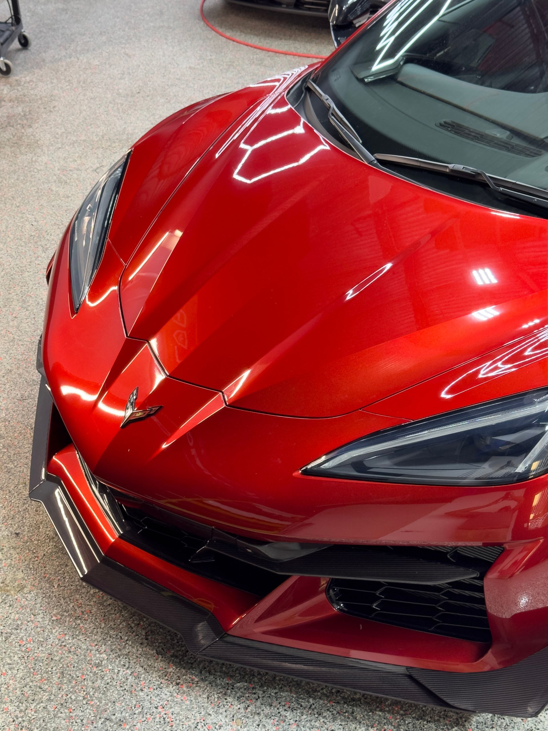 Red sports car, close-up of front. Shiny paint, black accents, indoors.