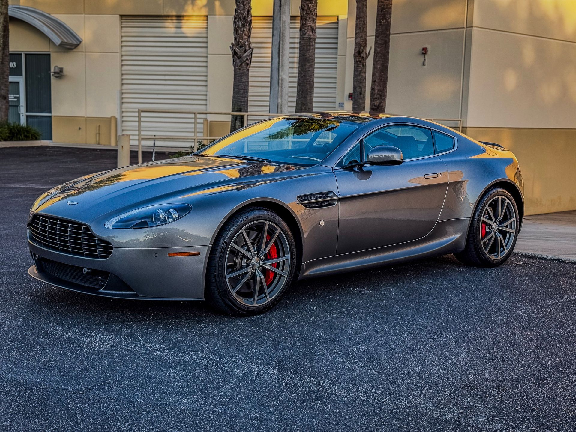 Gray Aston Martin sports car parked in front of a building with red brake calipers.