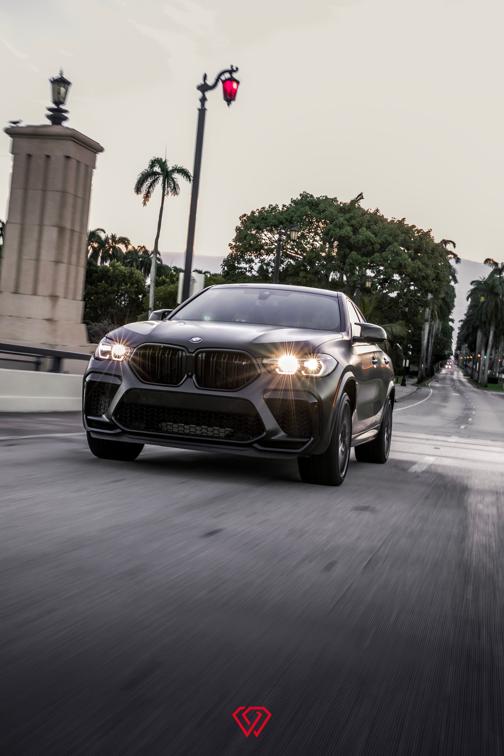 Black BMW SUV on a city street, headlights on, driving towards the camera.