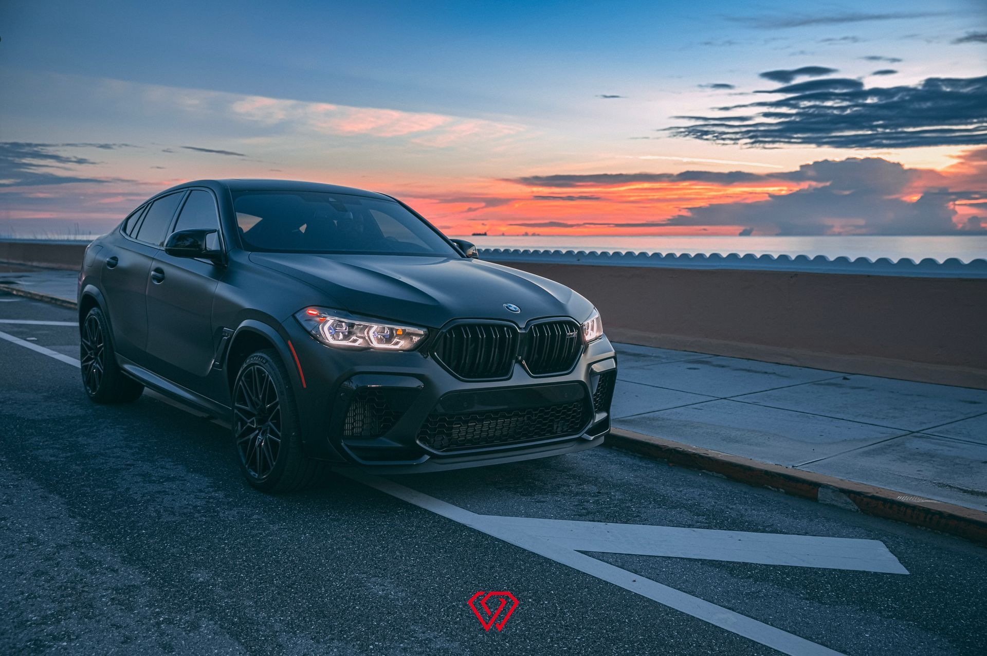 Black BMW X6 SUV parked on a road with a sunset in the background.