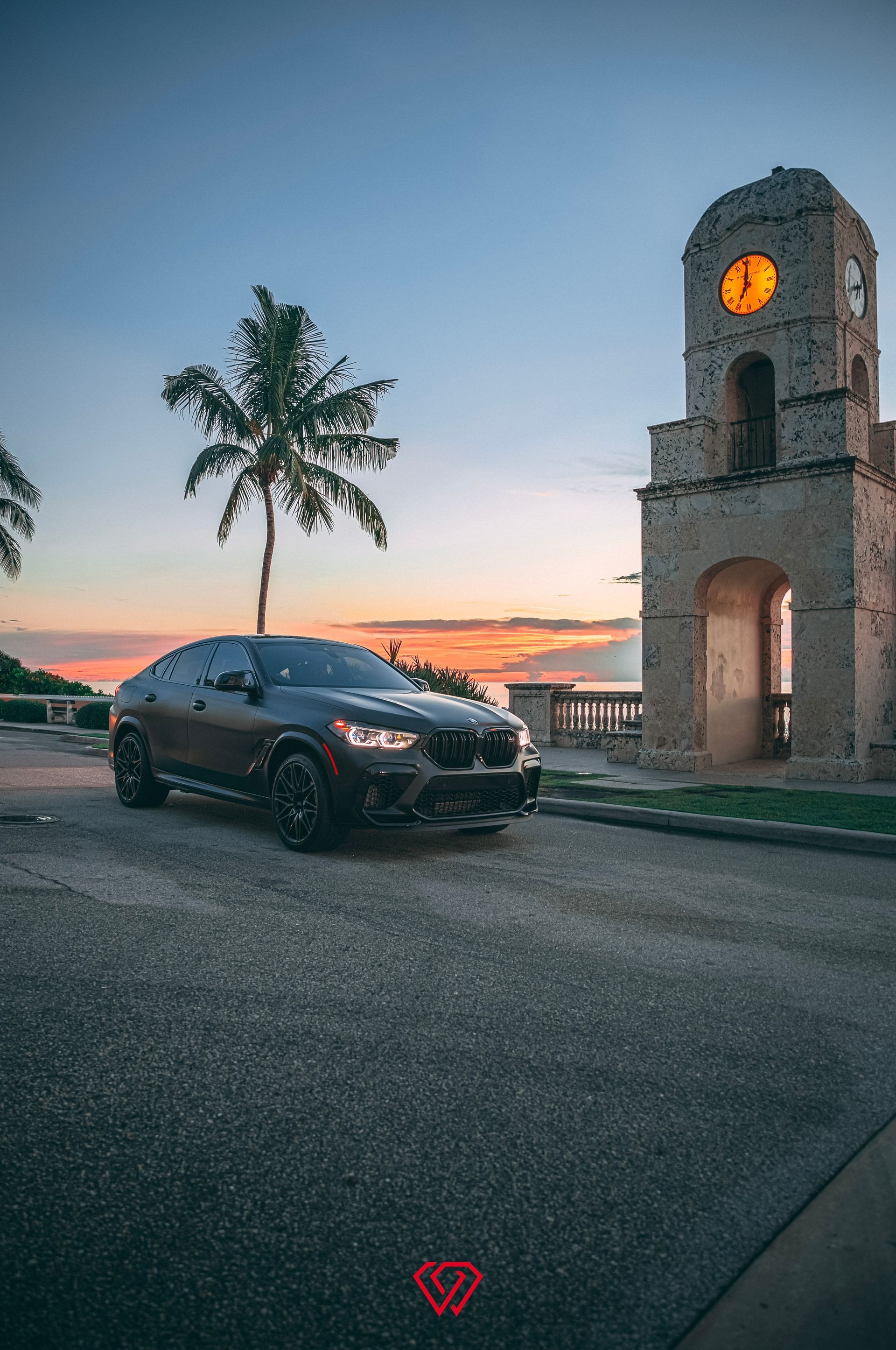 Black BMW SUV parked on road at sunset, next to a stone clock tower.