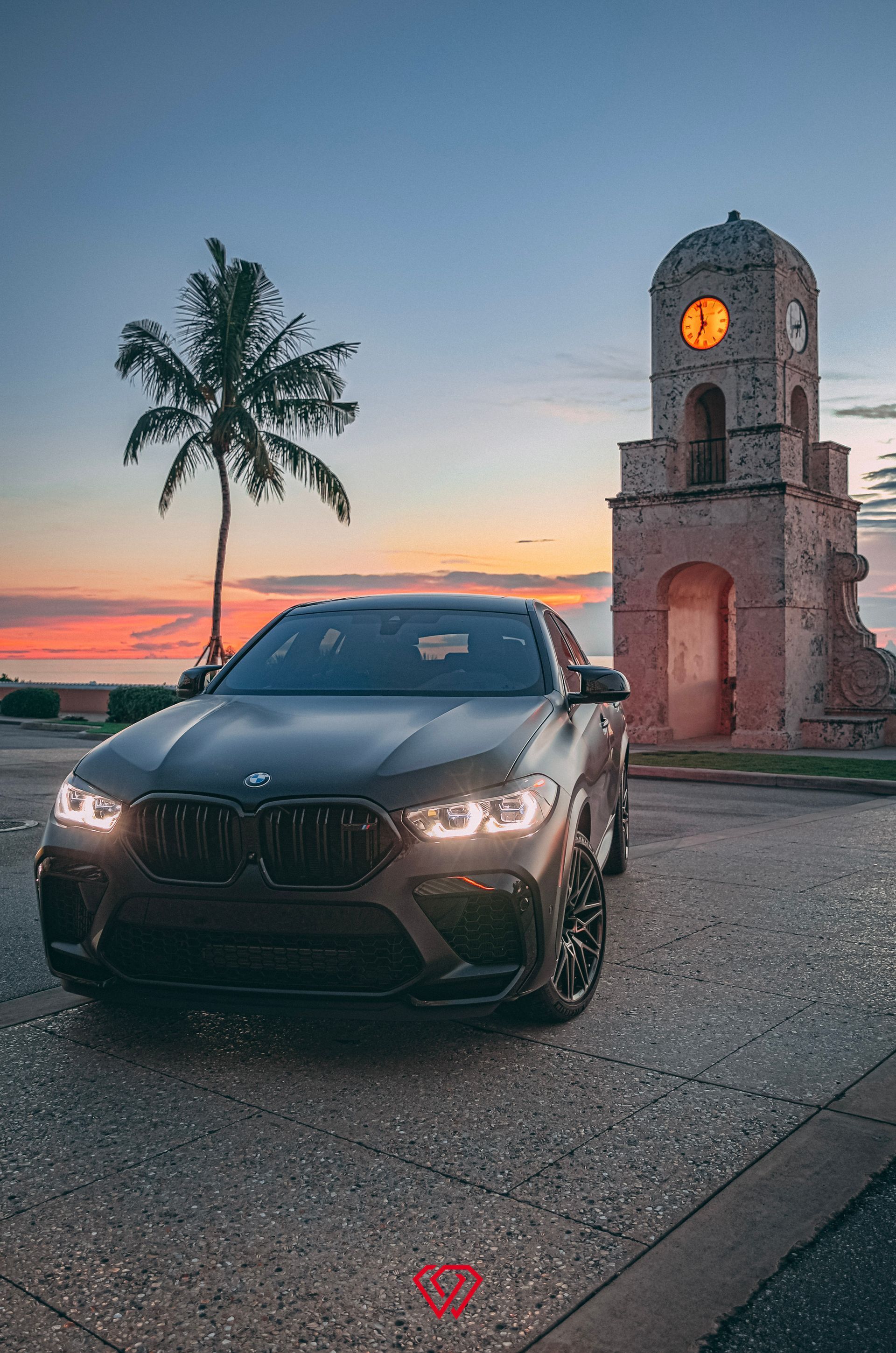 Dark gray BMW SUV parked in front of a clock tower at sunset.