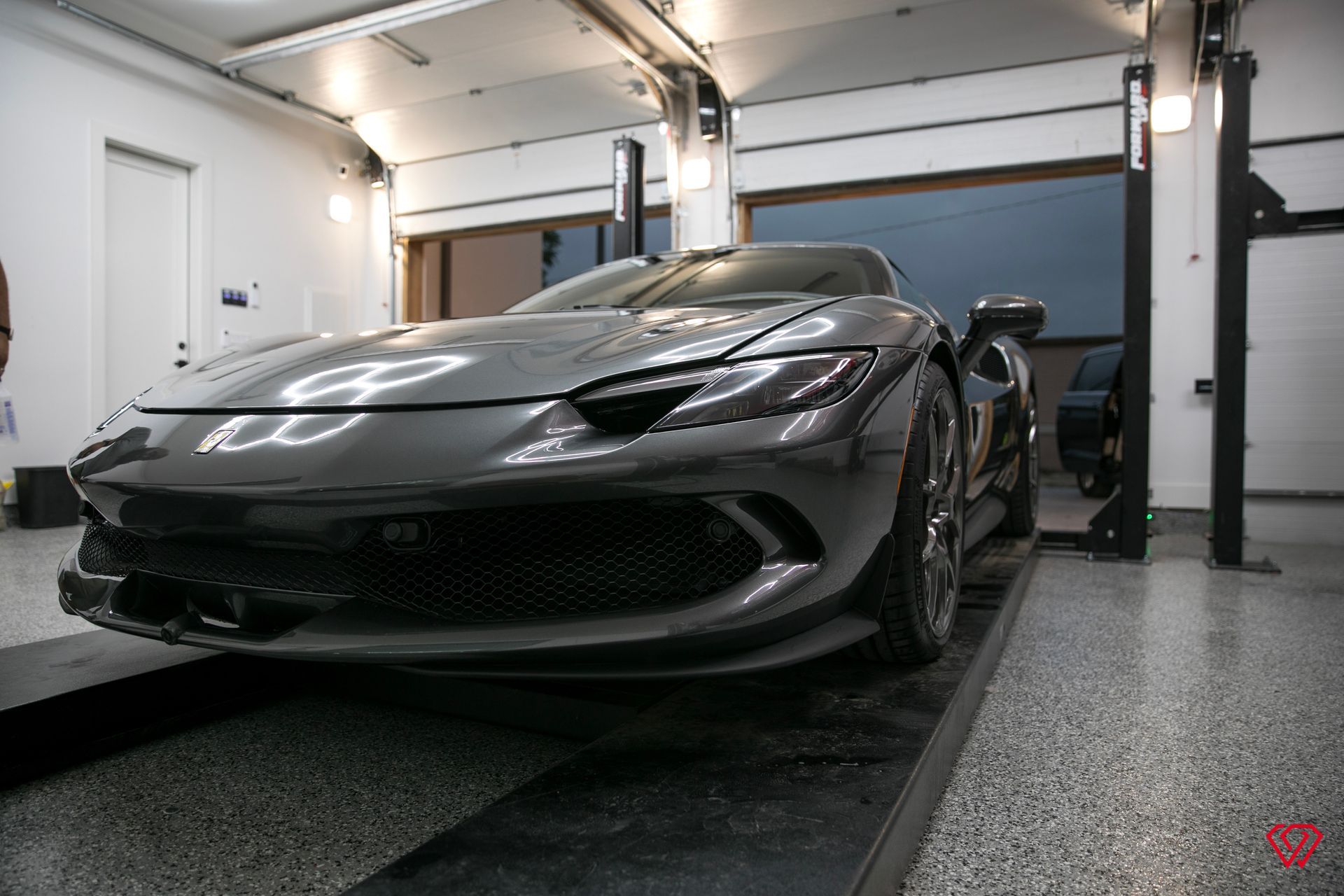 Gray sports car inside a well-lit garage, parked on a lift.