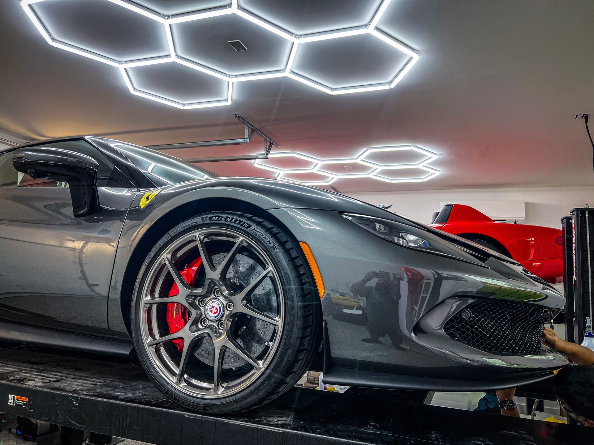 Gray sports car with red brake calipers parked under hexagonal lights.