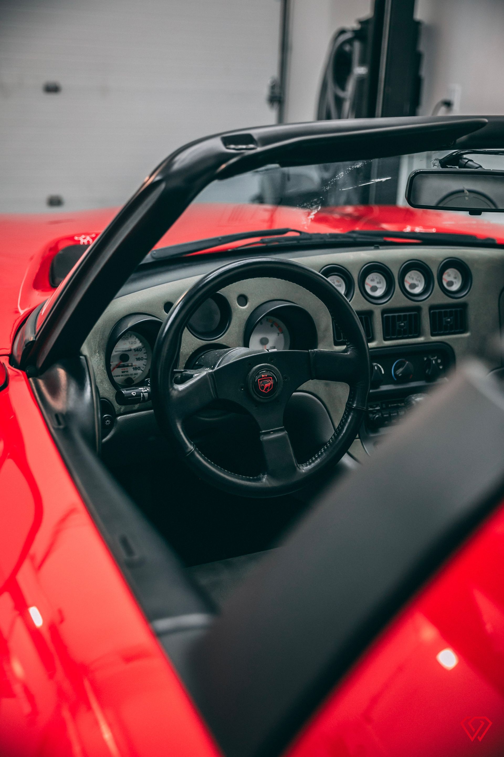 Red car interior with steering wheel, gauges, and windshield frame.