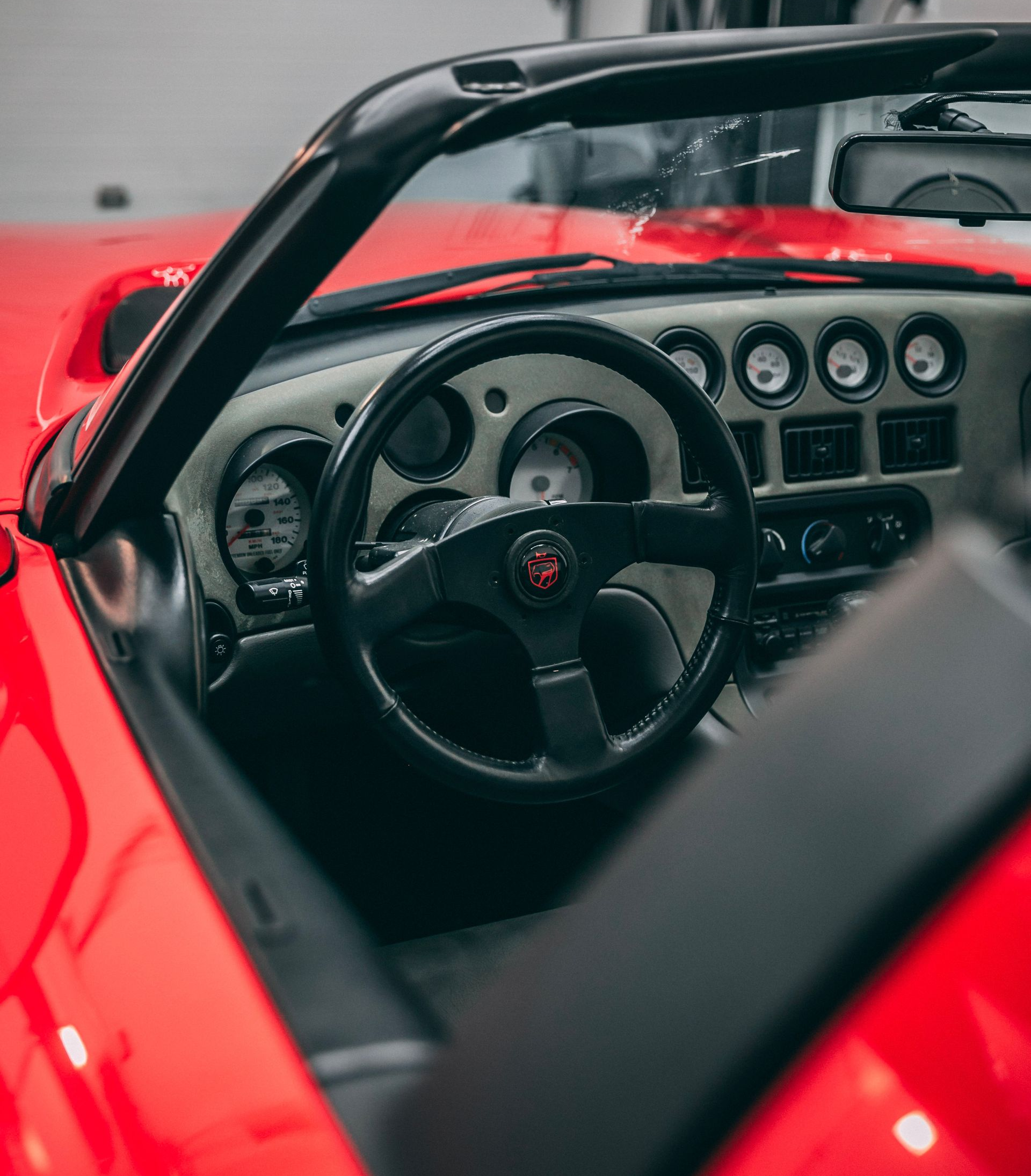 Red Dodge Viper convertible interior, black steering wheel, gauges, and dashboard.