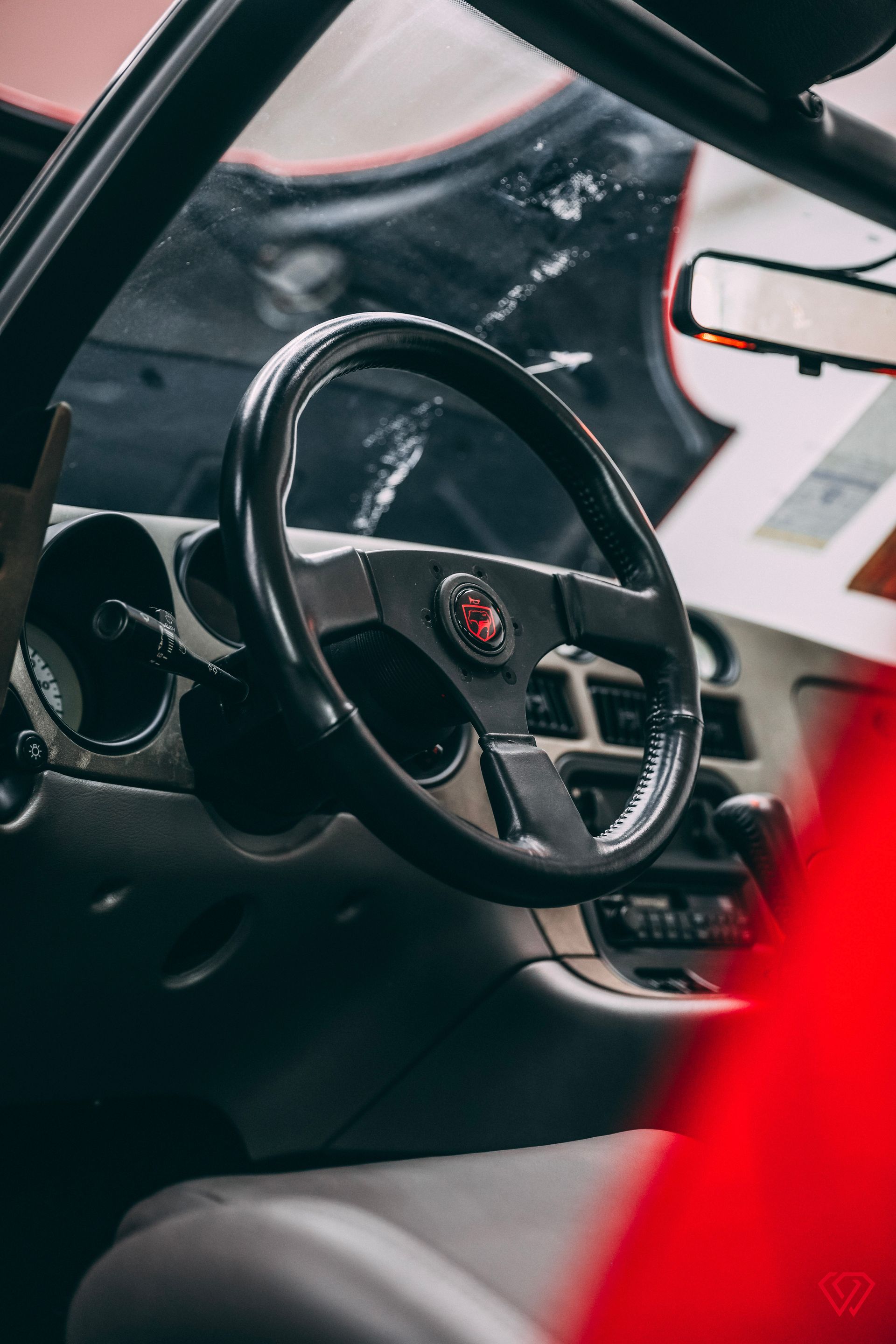 Black steering wheel inside a car, dashboard visible. Red car interior accents.