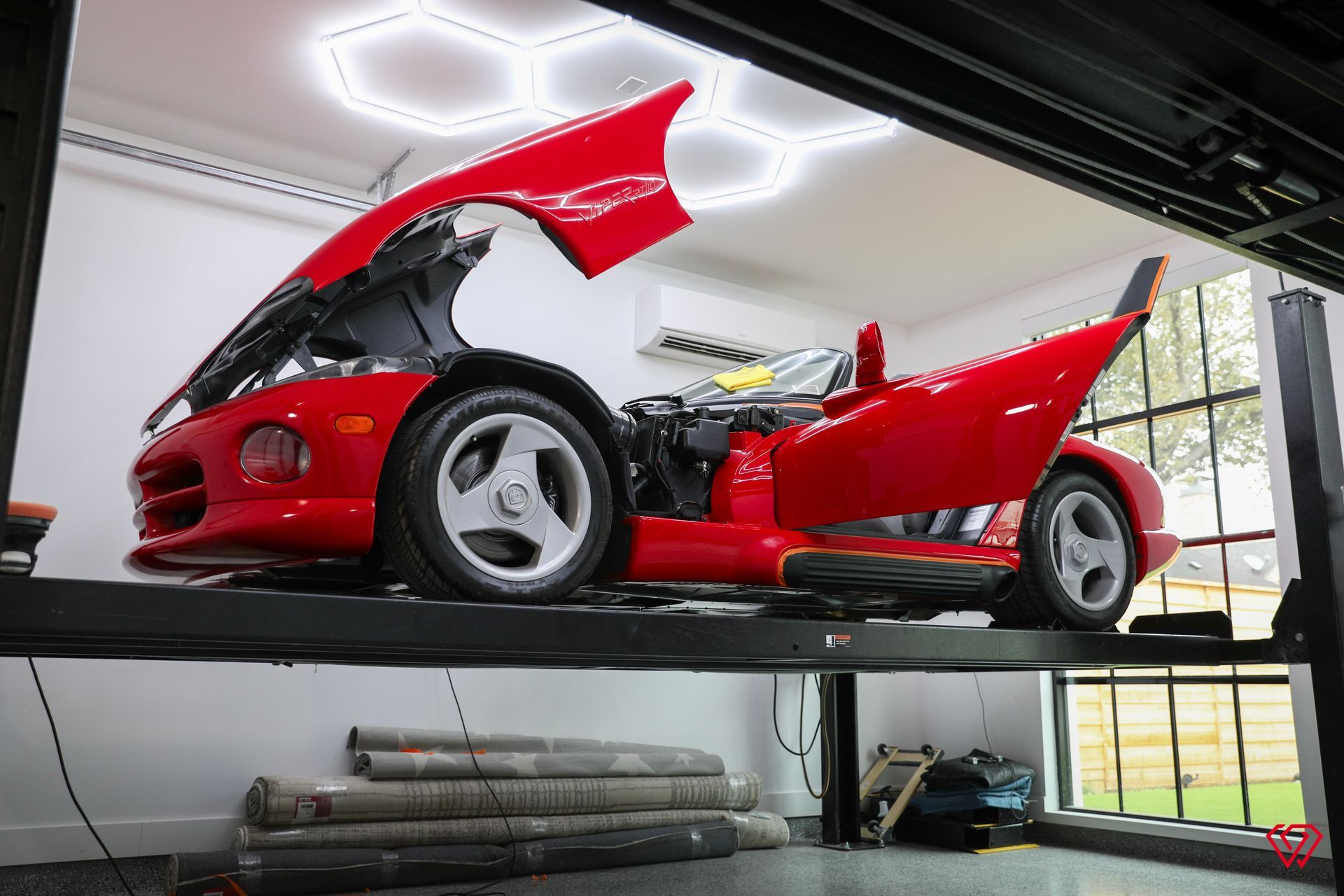 Red sports car on a lift, hood and door open, in a well-lit garage.
