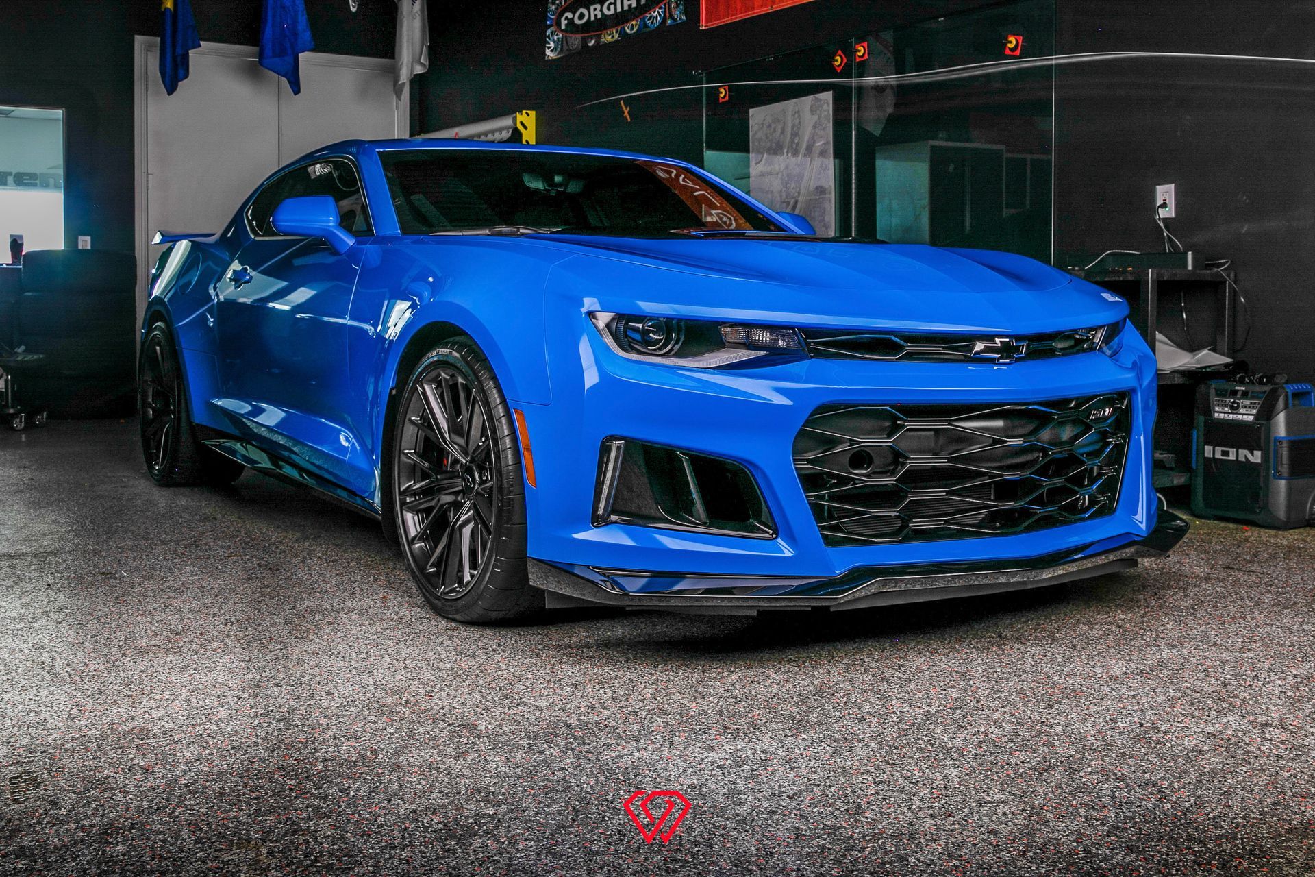 Blue Chevrolet Camaro sports car on a speckled floor inside a garage.