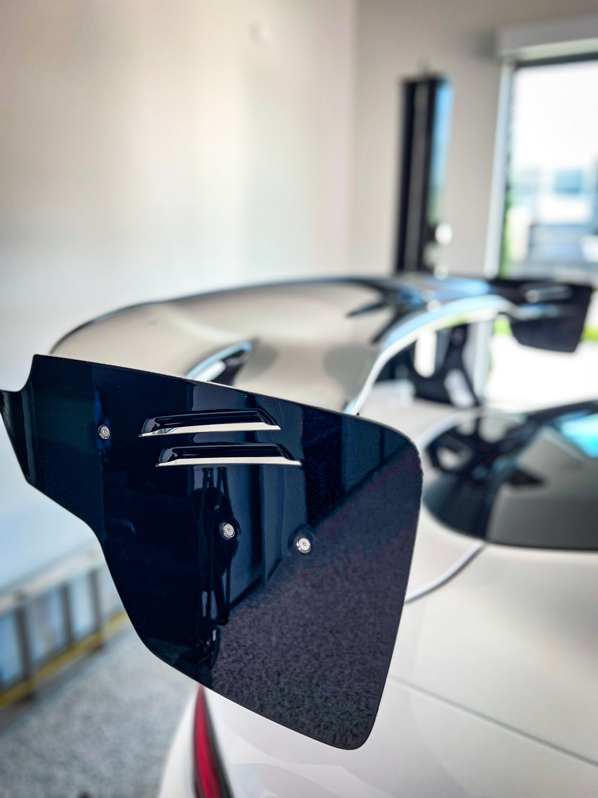 Black car spoiler on a white car, reflecting the garage interior.