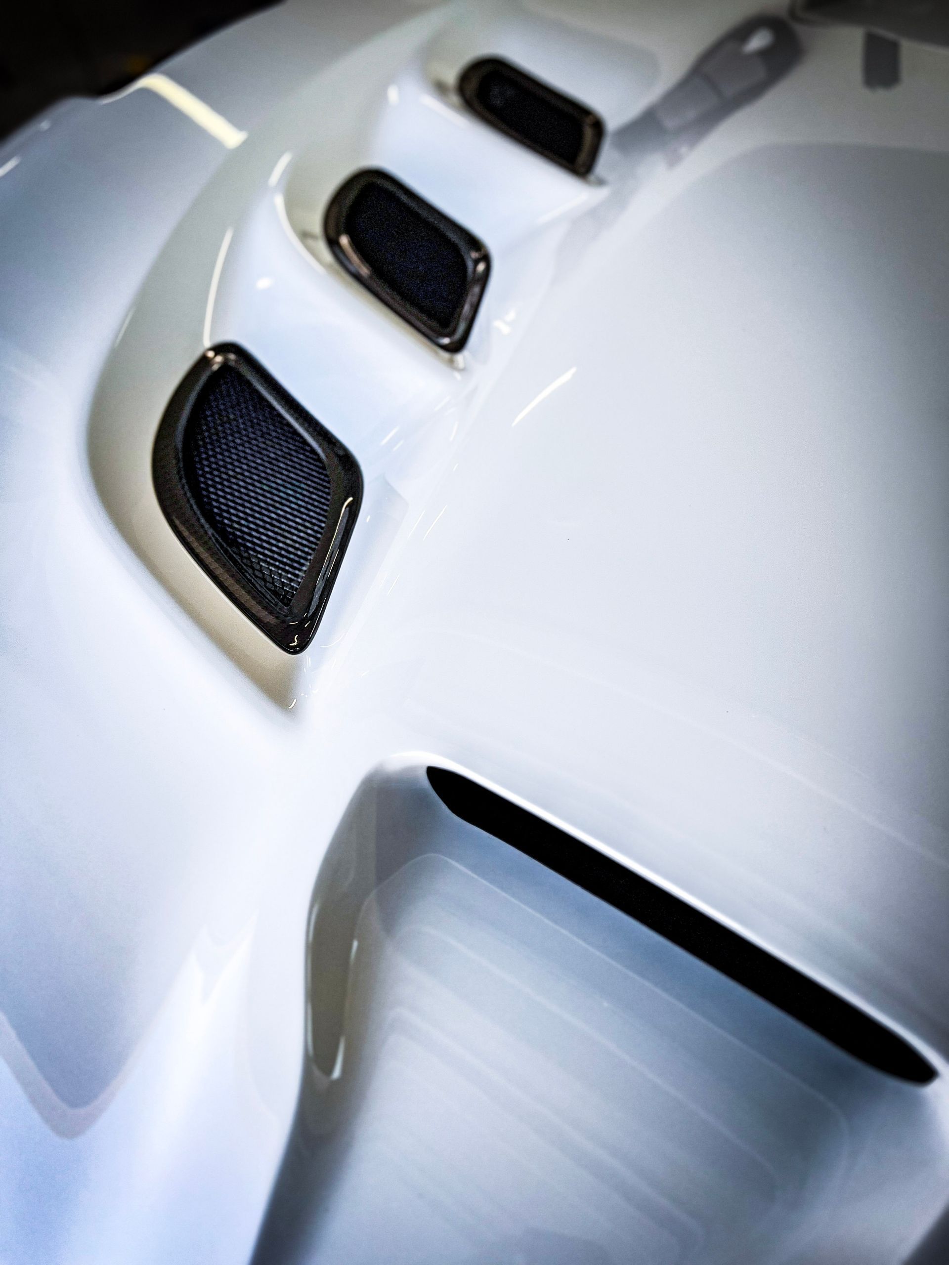 White car hood with three black mesh vents and a wide opening.