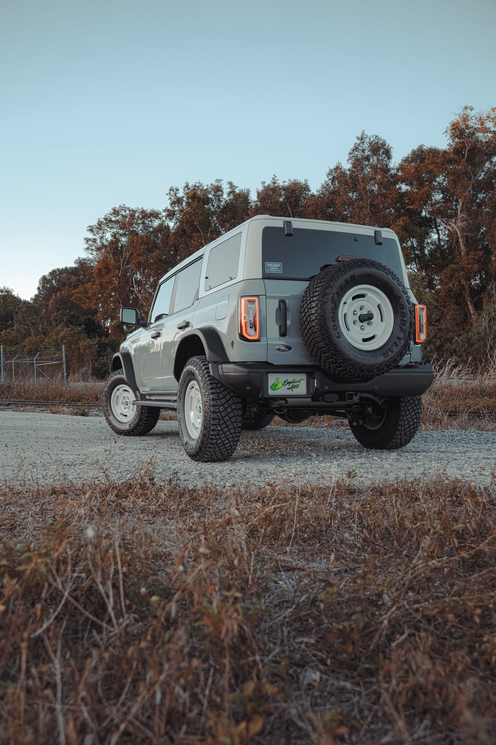 Gray Ford Bronco SUV on a gravel road, spare tire mounted, trees in background, daytime.