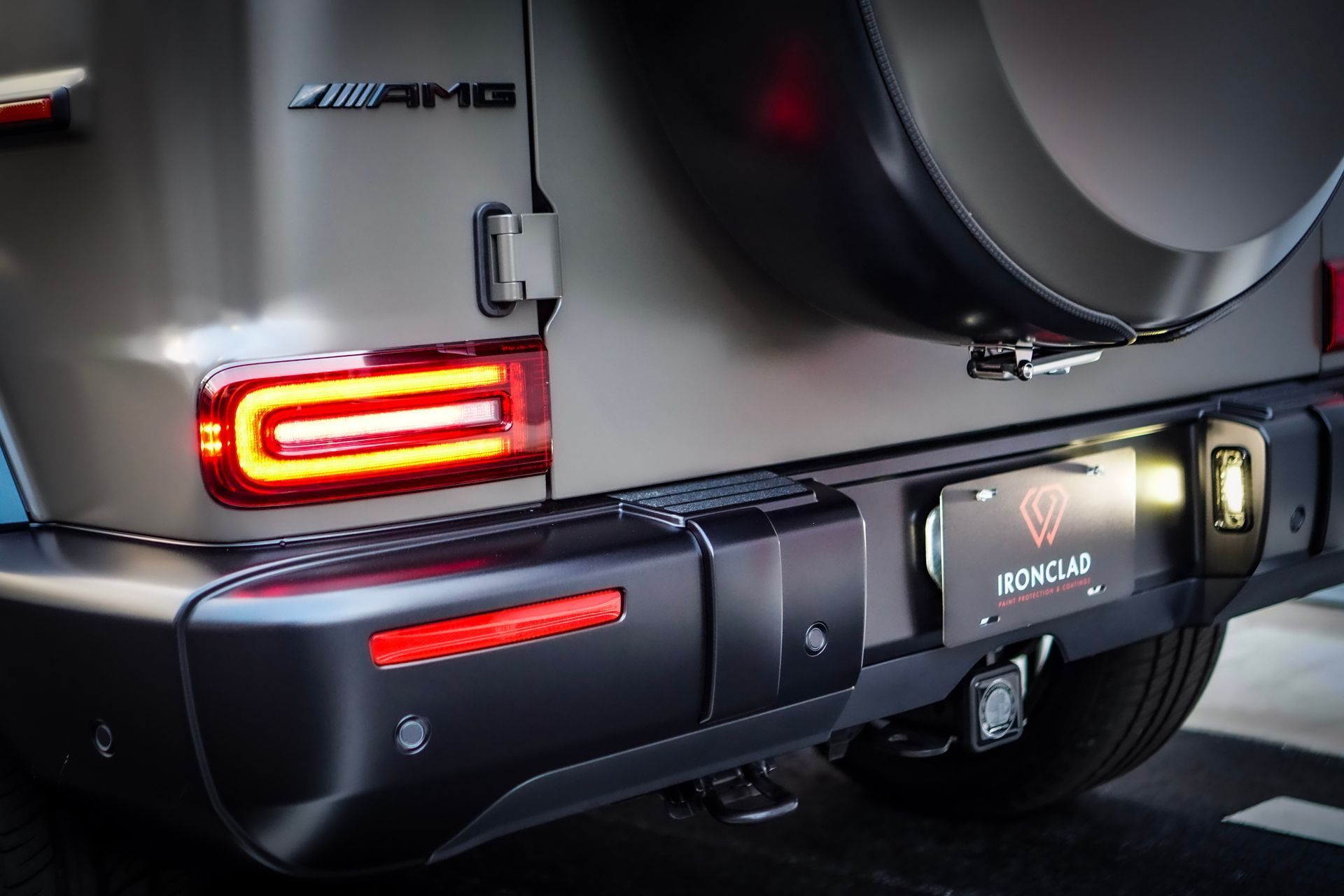 Rear view of a matte gray Mercedes-Benz G-Class AMG, with red taillights and spare tire.