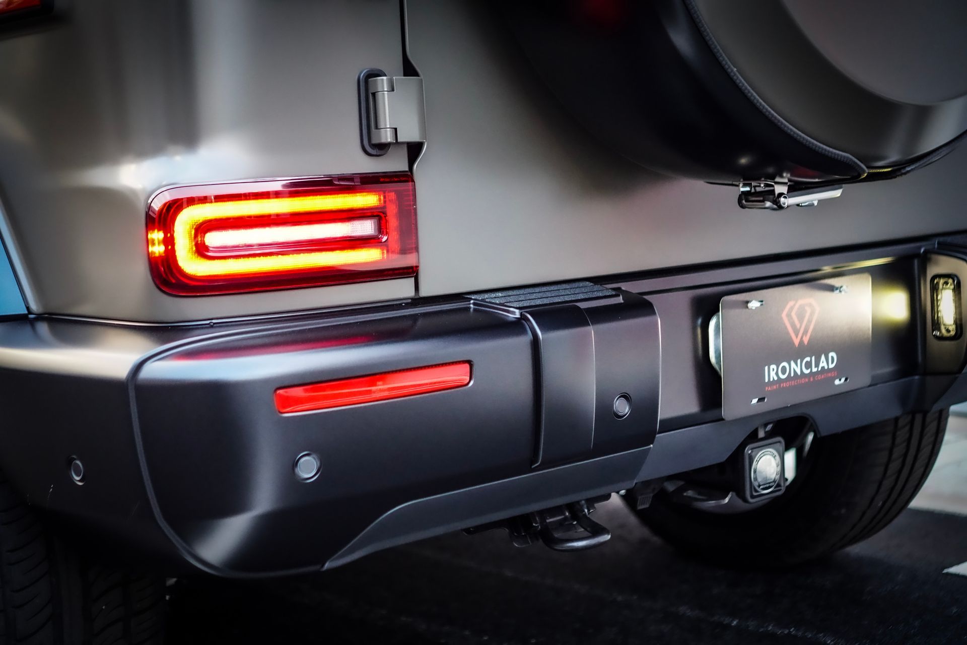 Rear view of a dark gray Mercedes-Benz G-Wagon, showing taillights, bumper, and spare tire.