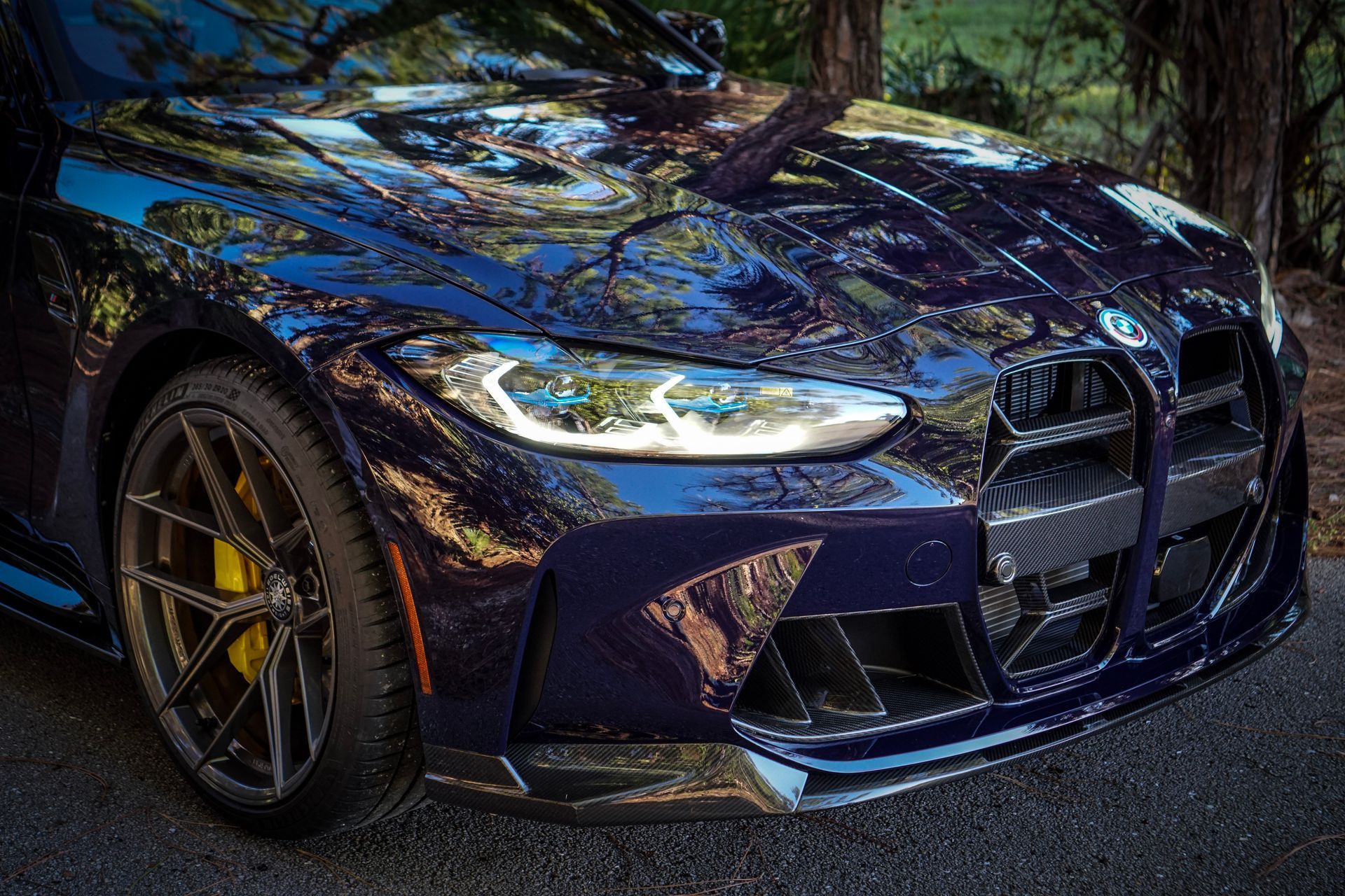 Dark blue BMW M4 sports car, front view, with yellow brake calipers, parked outdoors.
