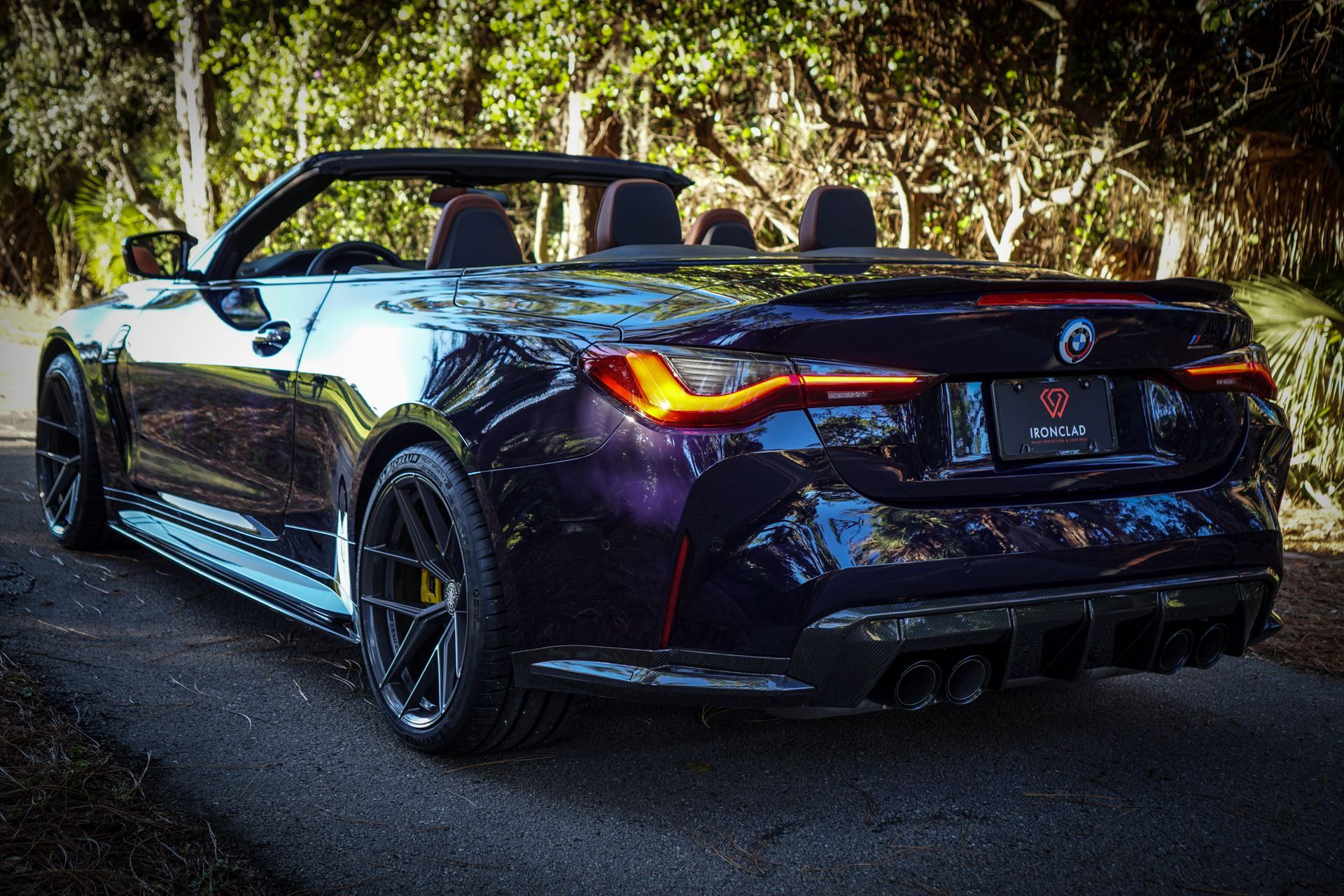 Dark blue convertible sports car on a road, top down, with black wheels and yellow brake calipers.