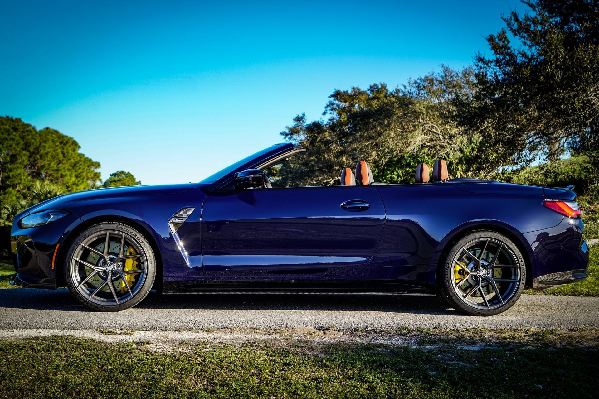 Dark blue convertible car parked on a road, top down, yellow brake calipers, sunny day.