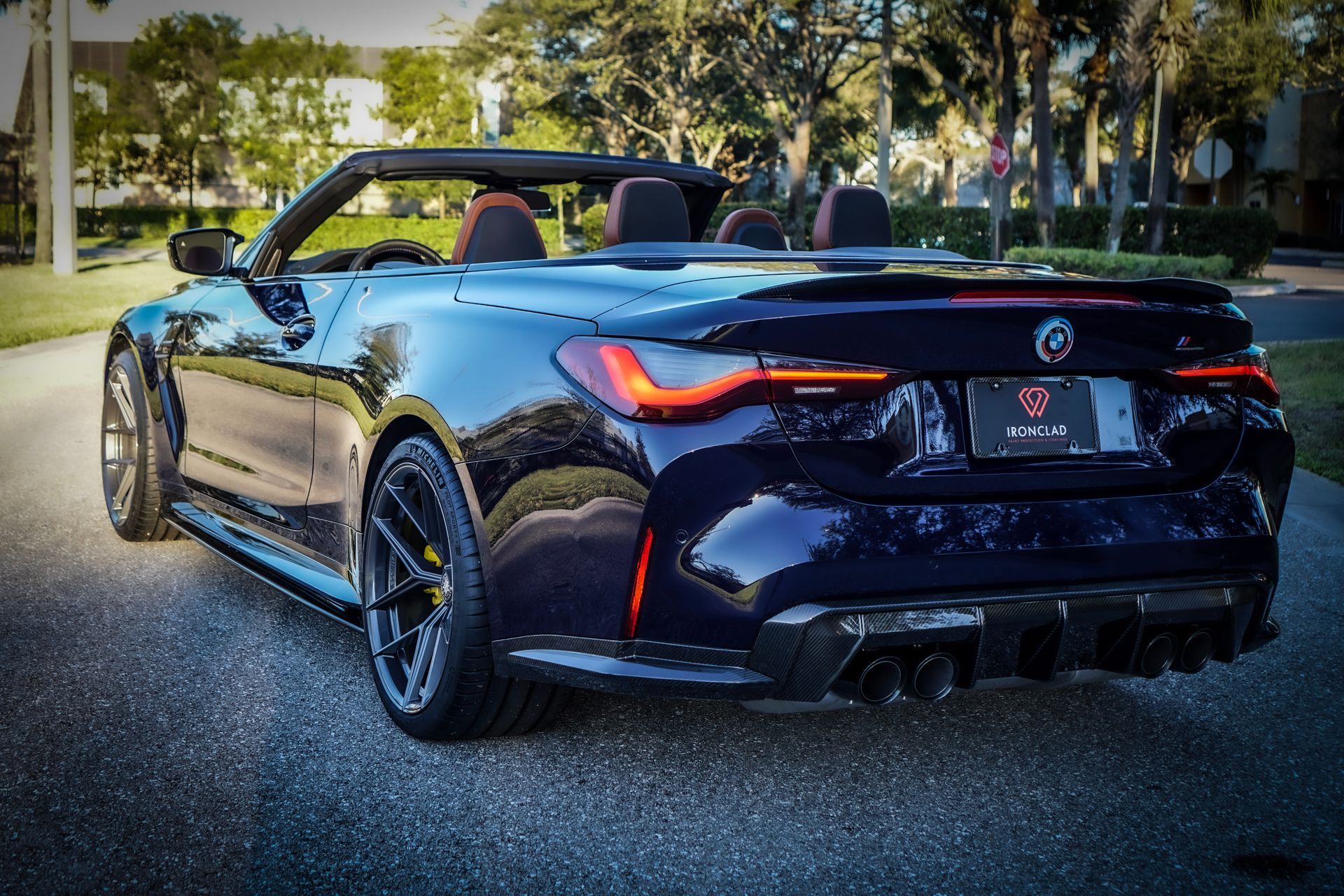 Dark blue convertible BMW on asphalt, rear view. Open top, sporty design, black wheels.