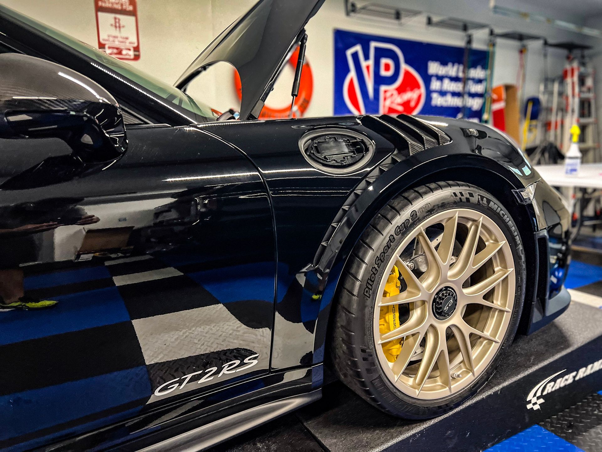 Black Porsche 911 GT3RS with gold wheels on a car lift; garage setting.