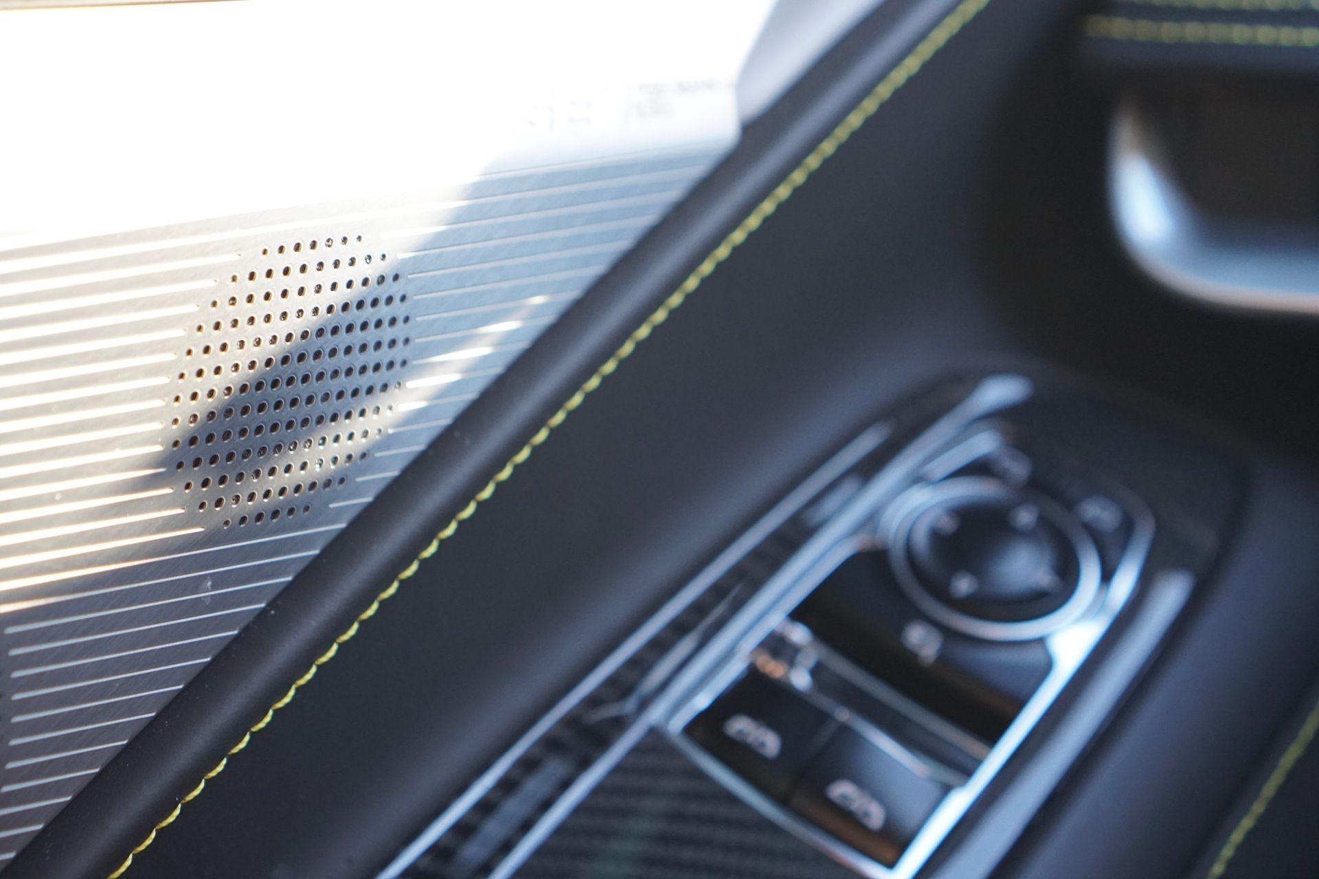 Car door panel detail, speaker grill, control buttons, black leather with yellow stitching.