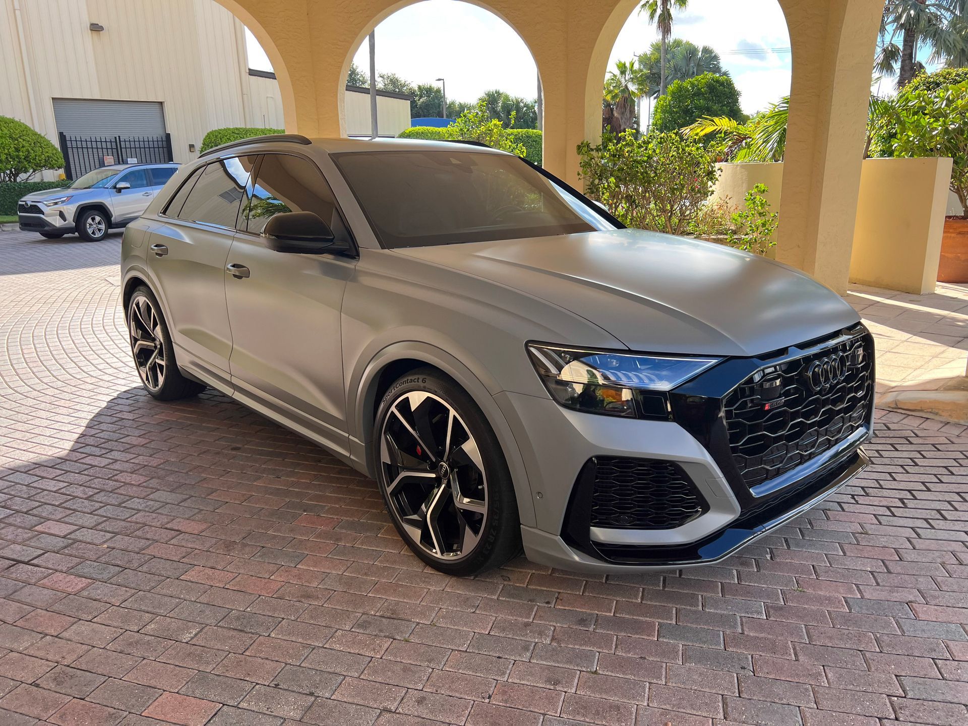 Gray Audi RS Q8 parked in a driveway, under an arched entrance.