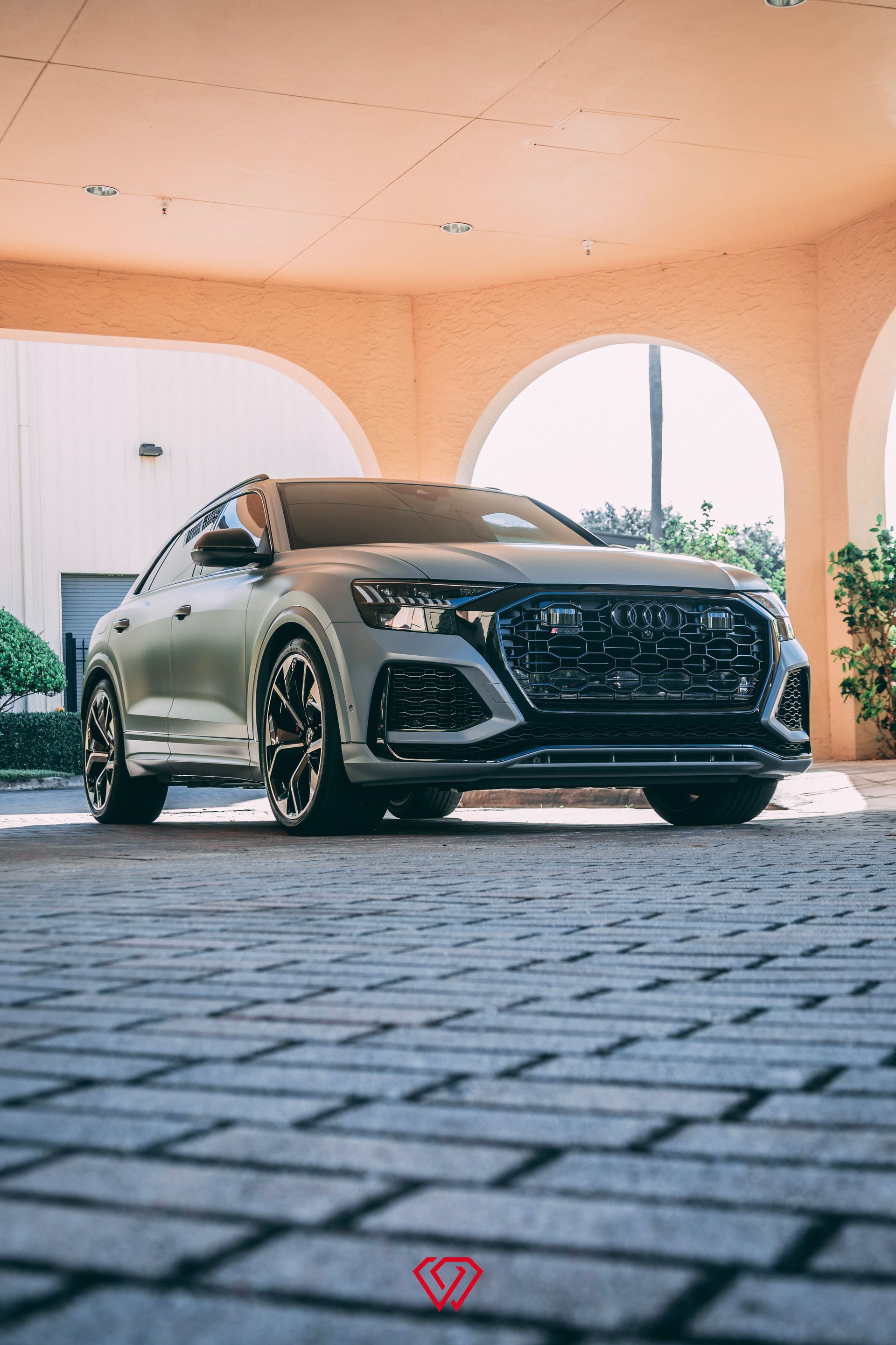 Gray Audi RS Q8 SUV parked under an arched entryway on a brick-paved surface.