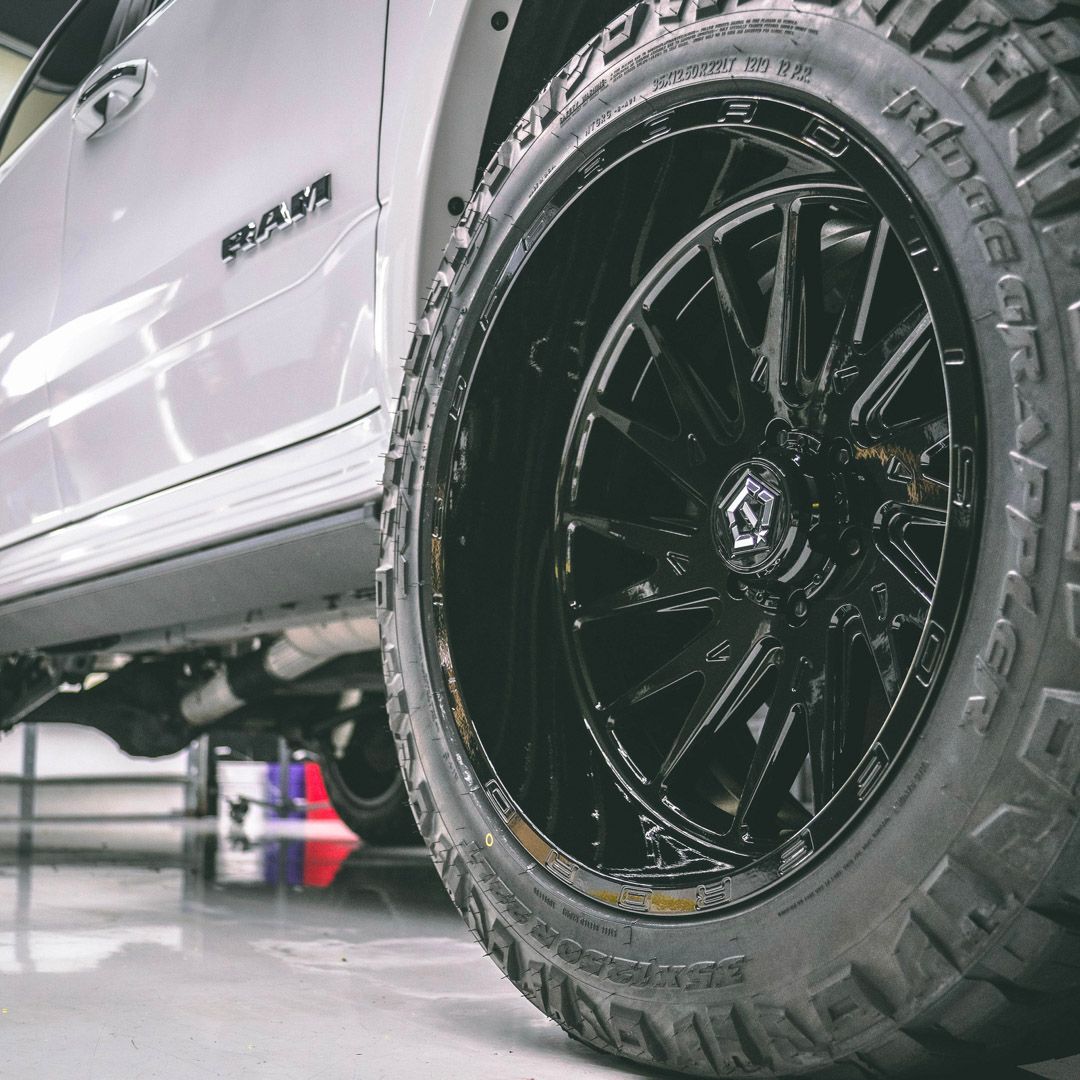 Close-up of a white truck with a glossy black wheel and rugged tire.