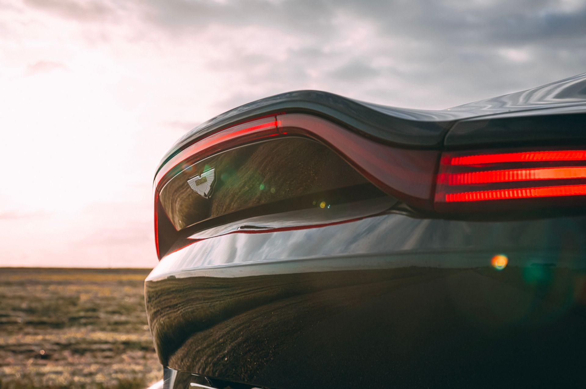 Black car's taillight and rear body, with red lights against a sunset sky.
