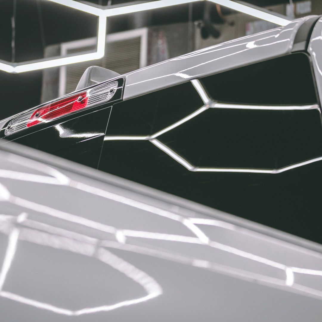 Close-up of a futuristic car's rear, showcasing a red light and a geometric patterned background.