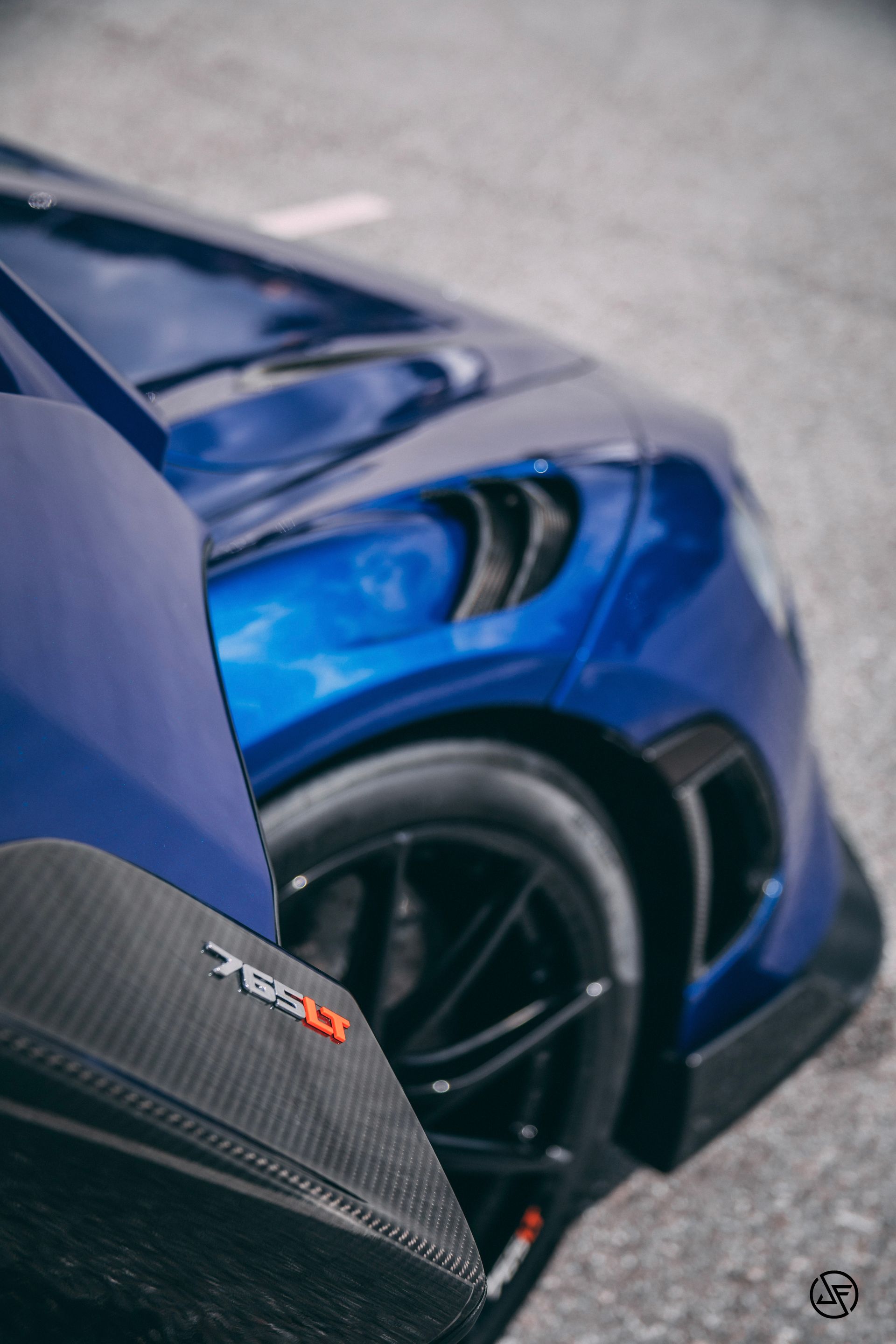 Blue sports car with black rims, and a partially open door with carbon fiber accents.