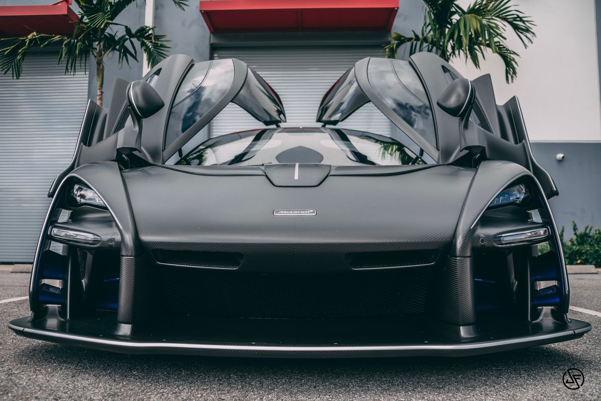 Dark gray McLaren Senna with open doors, parked in front of a building.